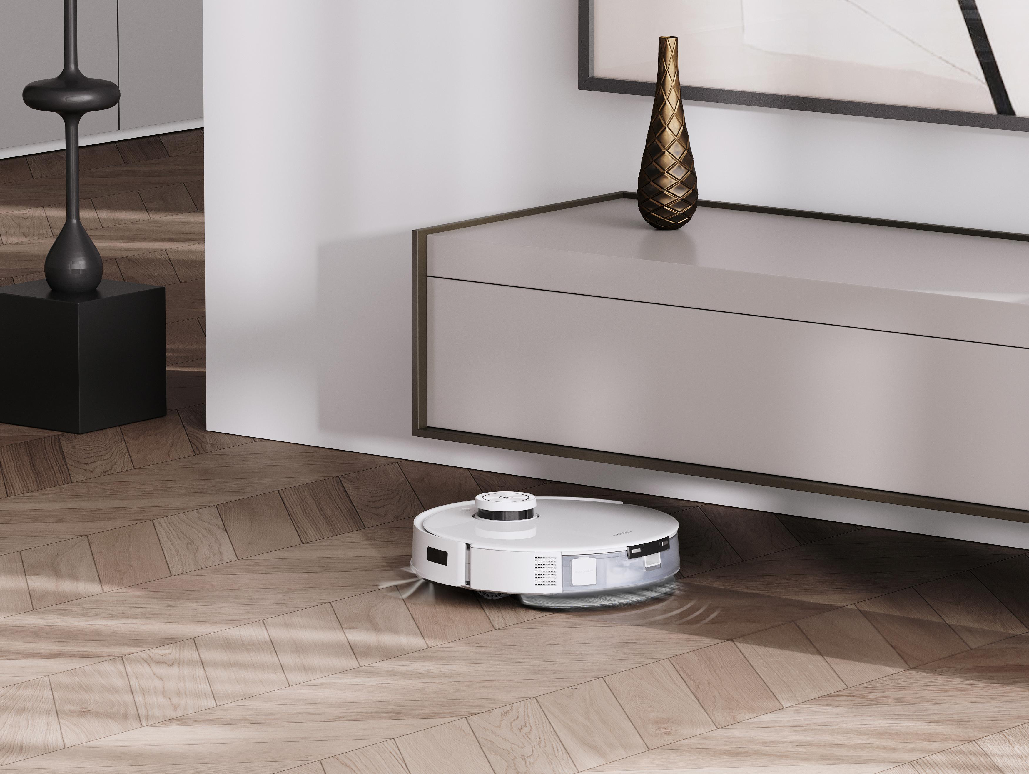 Ein weißer Roboter-Staubsauger auf einem Holzboden, mit einer dekorativen Vase.