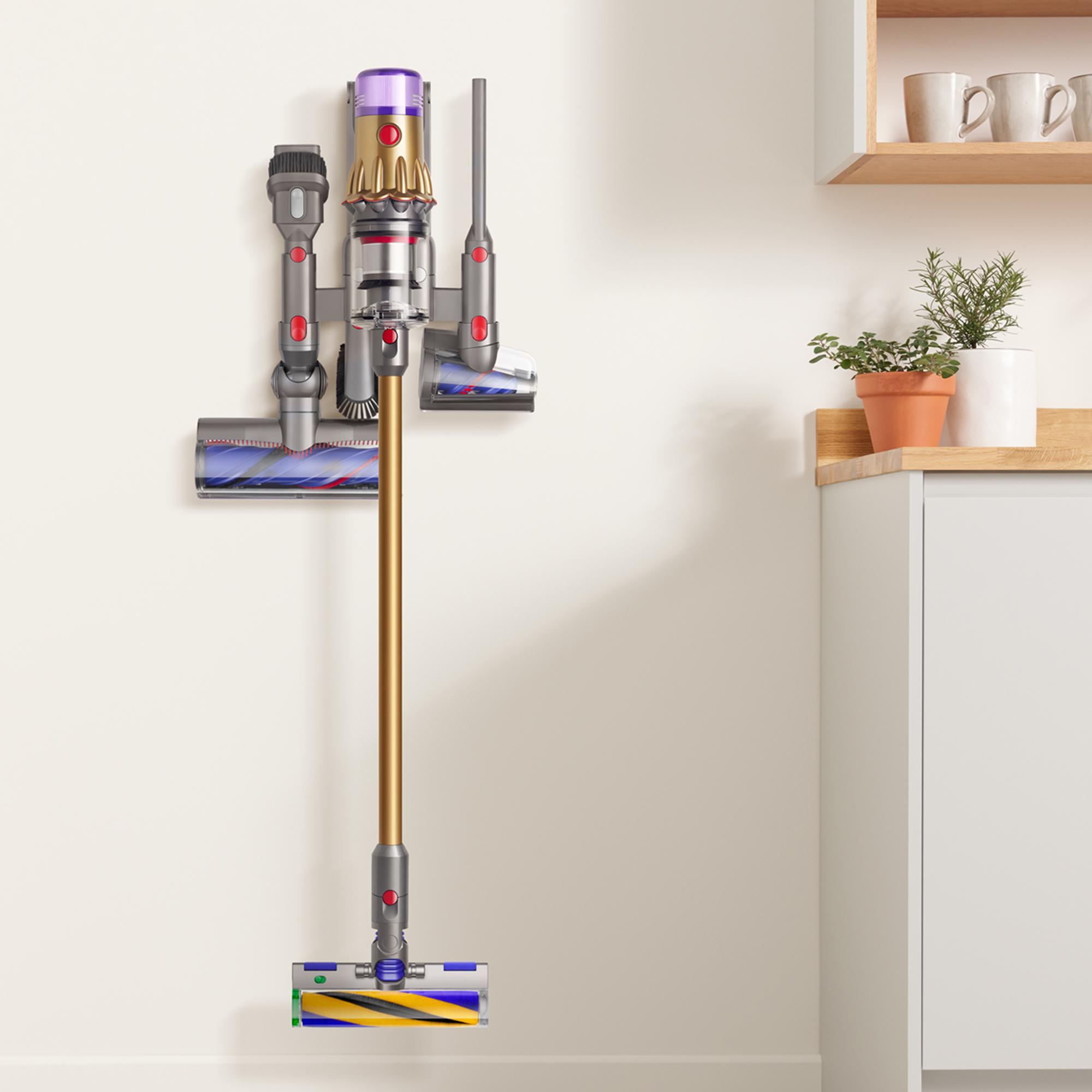 Ein Dyson-Staubsauger an einer Wand in einem hellen Raum montiert. Verschiedenes Zubehör ist befestigt.