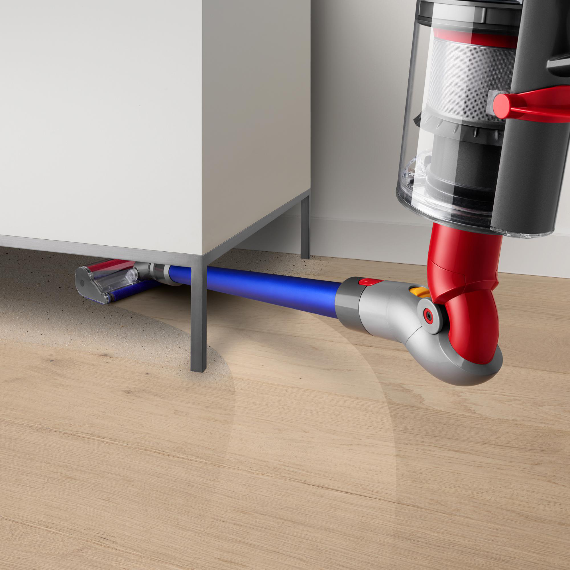 Ein blauer und roter Staubsauger unter einem weißen Schrank, der einen Holzboden reinigt.