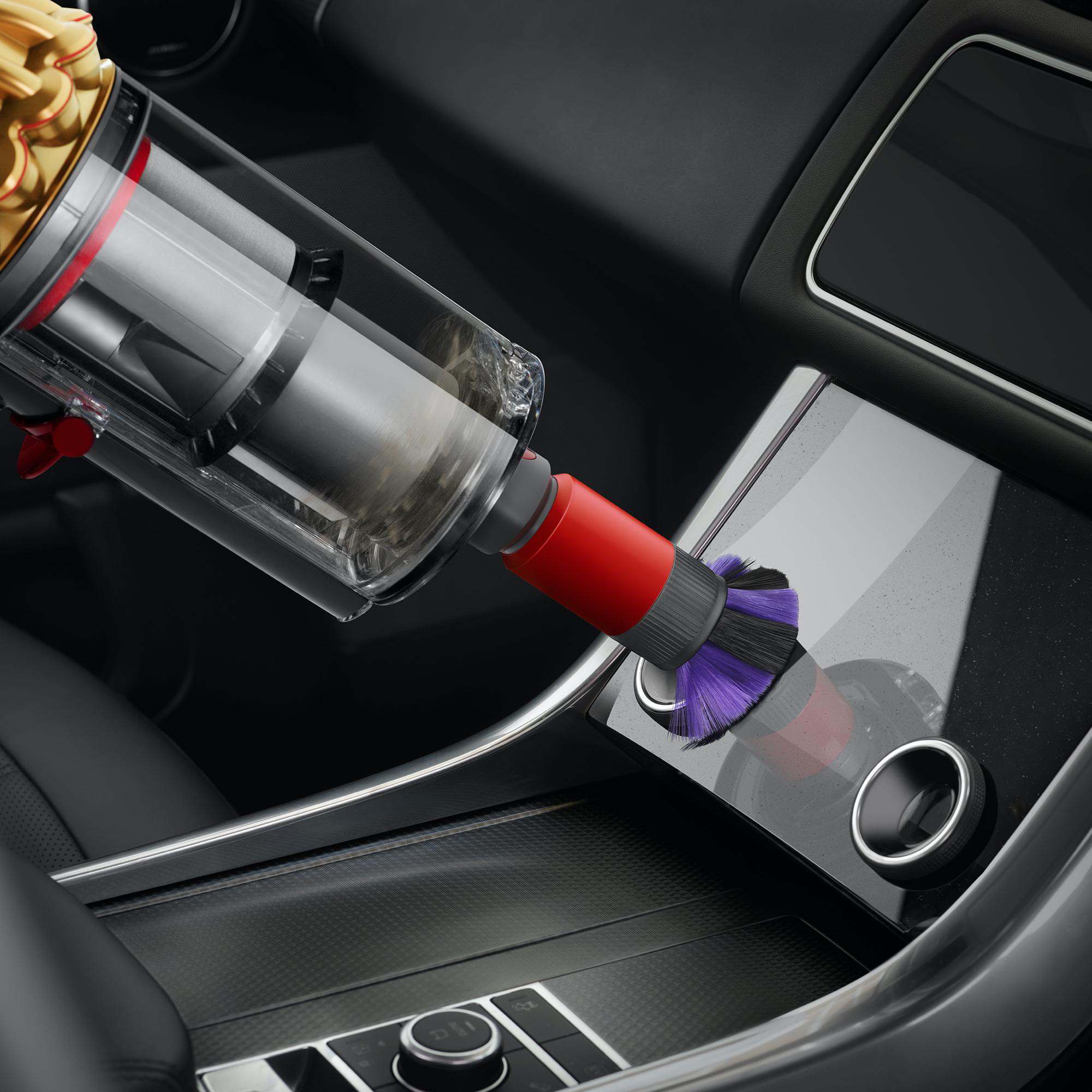 Ein Staubsauger reinigt das Armaturenbrett eines Autos. Die Bürste ist rot und grau. Der Innenraum ist schwarz.