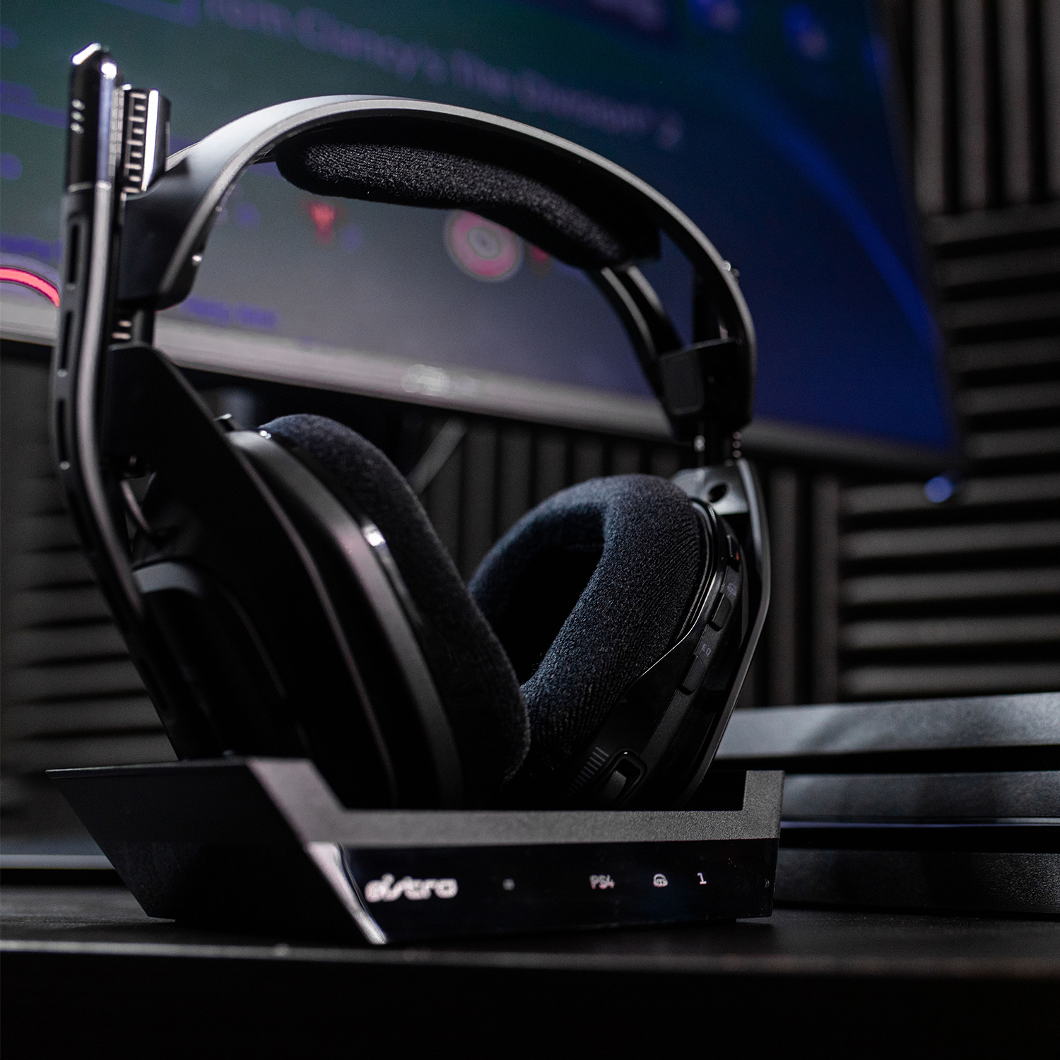 Casque de jeu Astro sur une base de chargement, avec une console et une TV en arrière-plan.