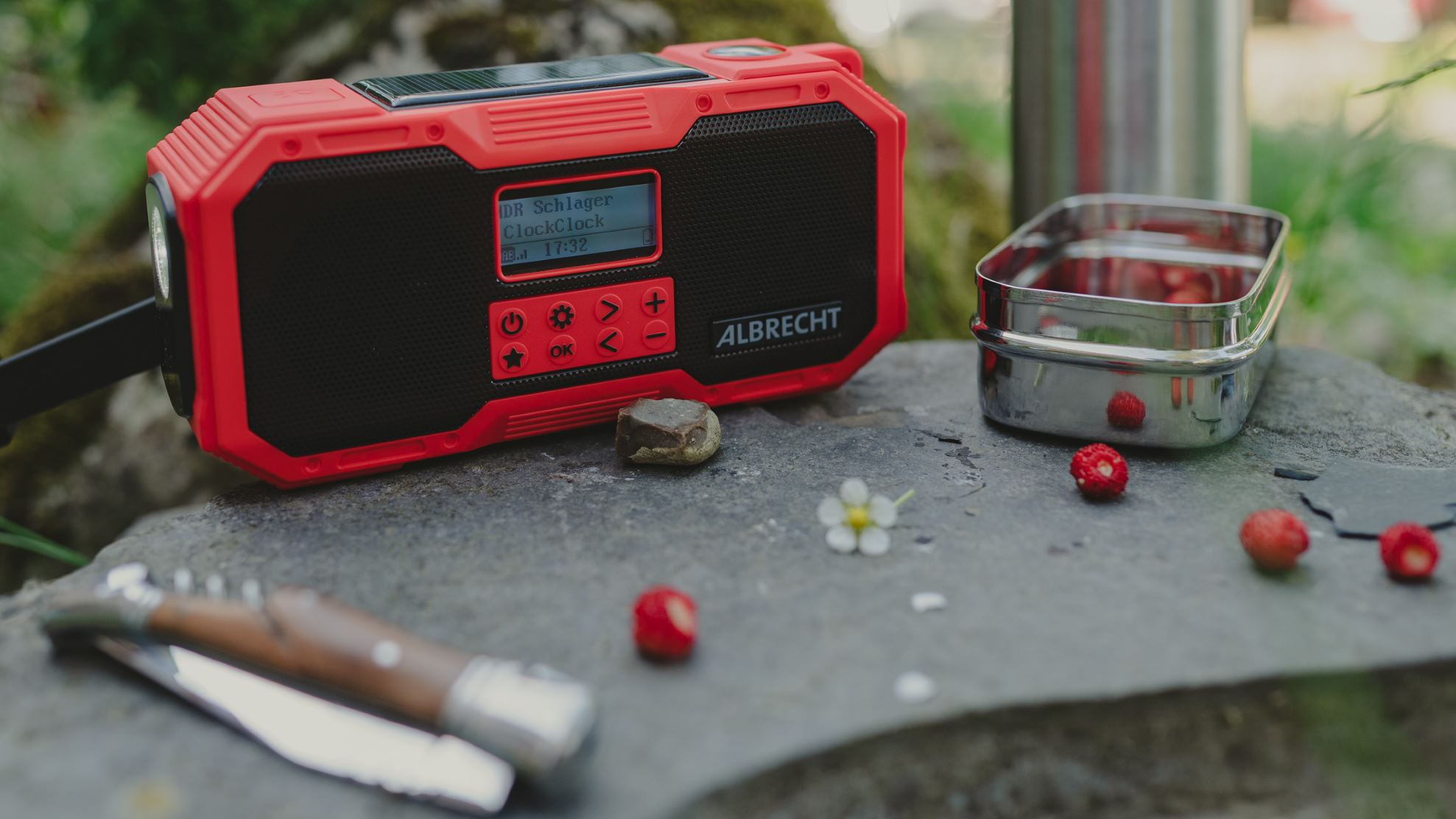 Rotes und schwarzes tragbares Radio auf einem Felsen mit Essen und einem Messer.