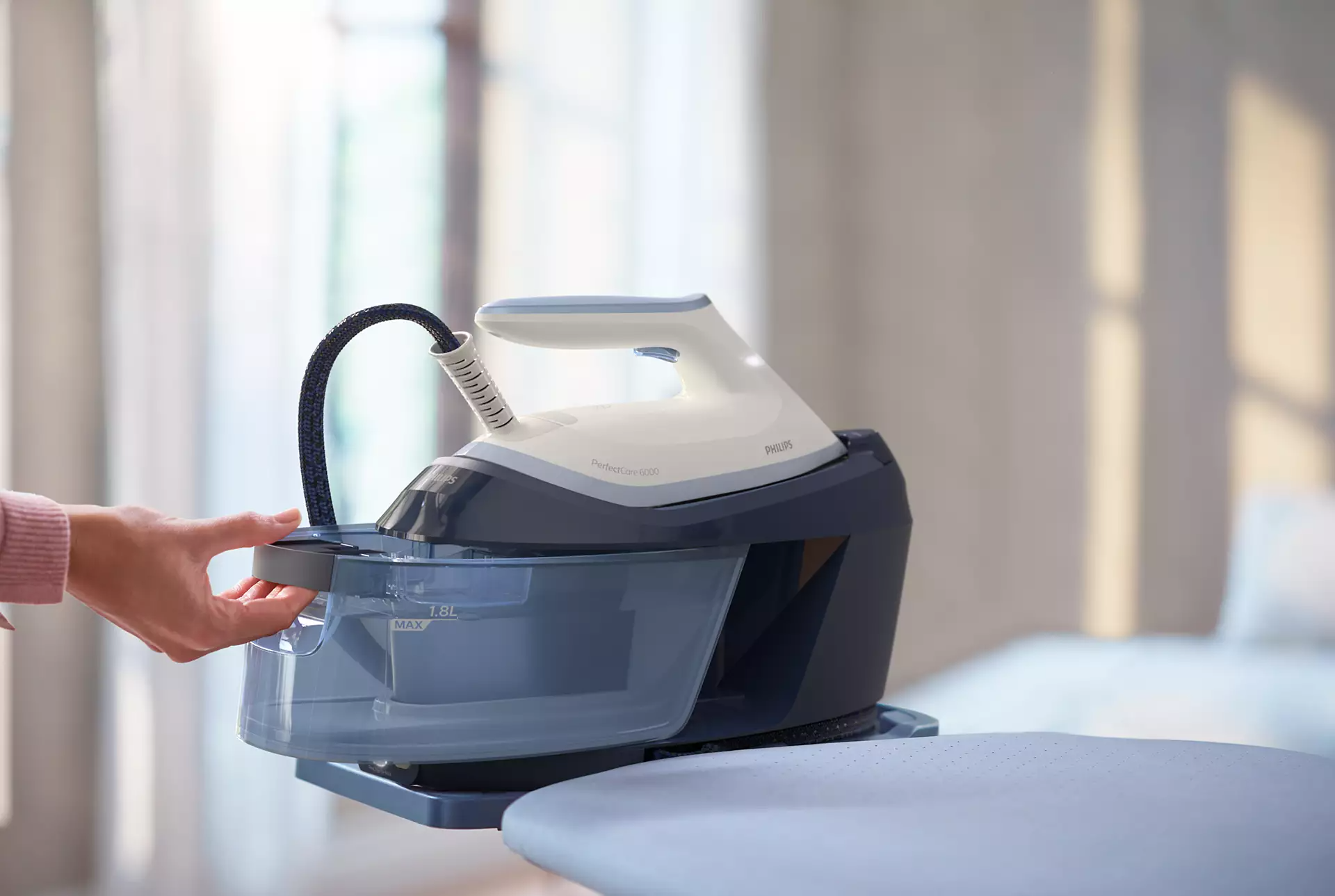 Egy személy keze vizet ad egy Philips PerfectCare gőzfejlesztős vasalóhoz.