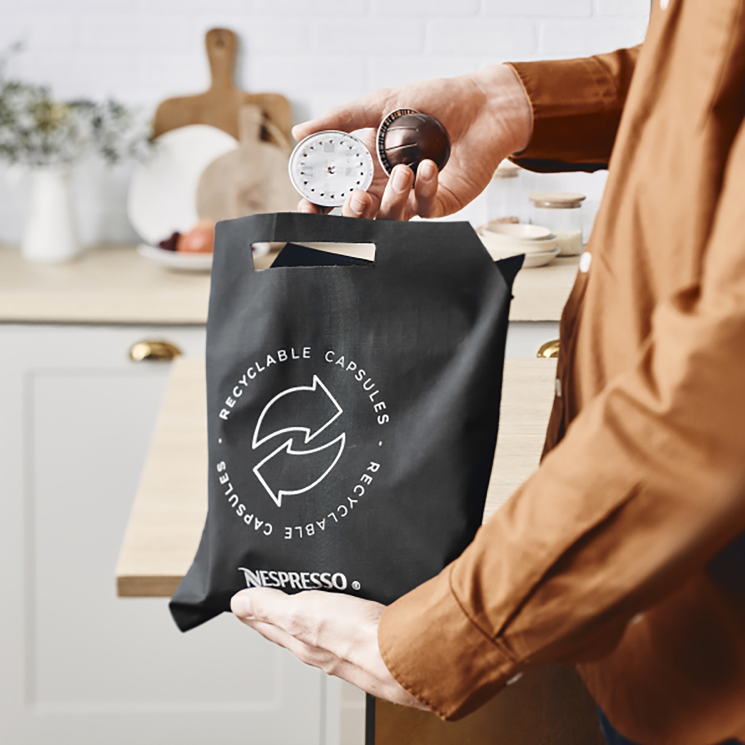 A person holding coffee capsules and a Nespresso recycling bag.