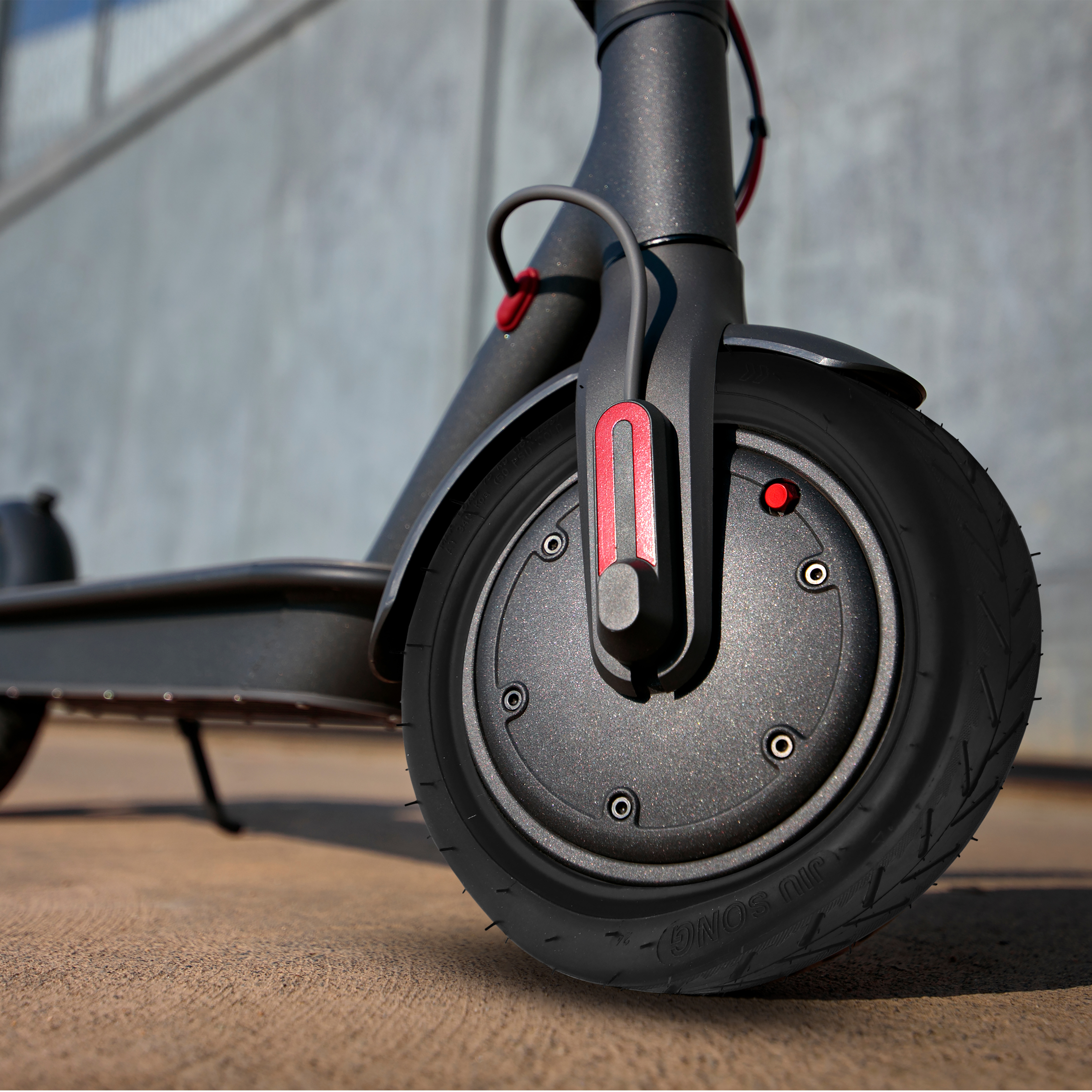 Ruota di scooter elettrico nera con pneumatico, accento rosso, su cemento, sfondo grigio.