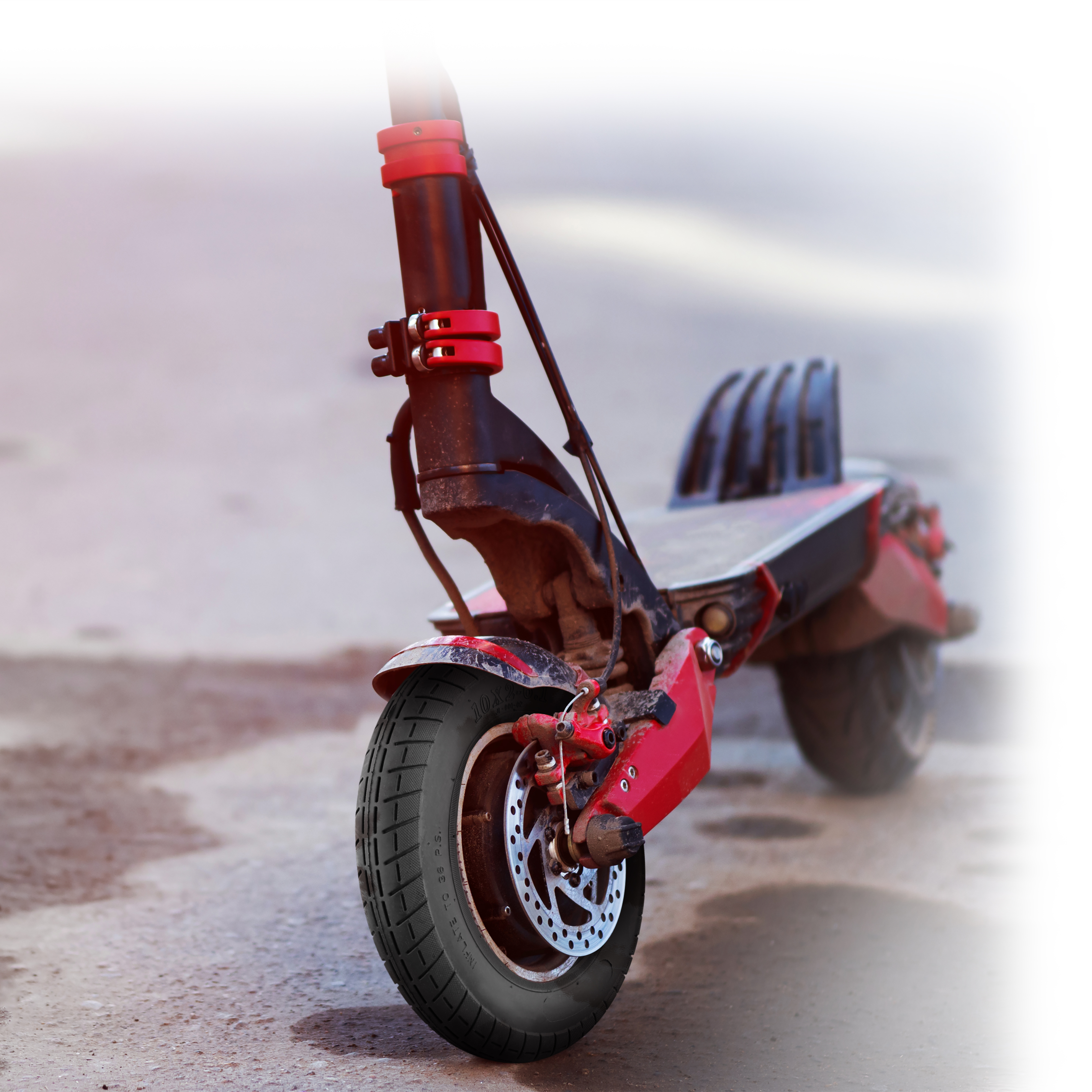 Scooter elettrico rosso e nero sull'asfalto. Lo pneumatico anteriore è a fuoco. Sfondo sfocato.
