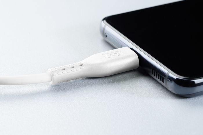 Un cable de carga blanco insertado en un smartphone negro, sobre una superficie gris.