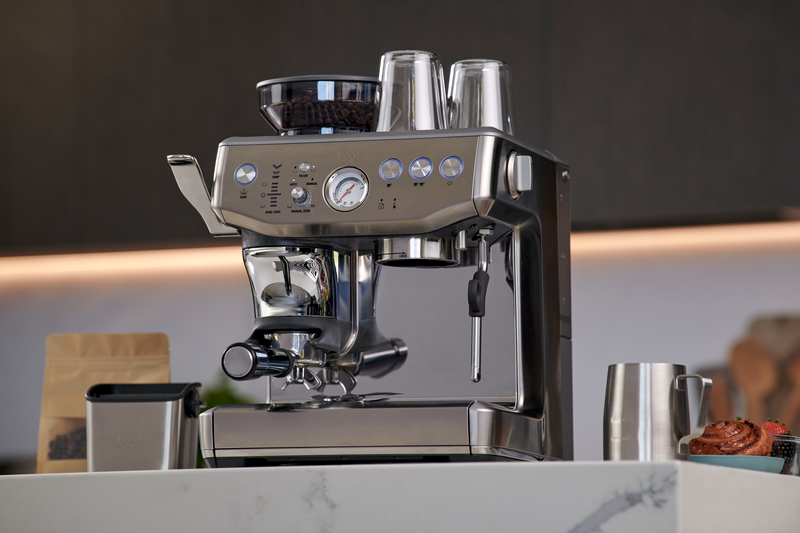 Machine à expresso argentée avec accessoires, sur un comptoir blanc.