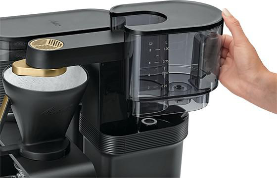 Nahaufnahme eines schwarzen Kaffeeautomaten mit einer Hand, die einen Behälter hält.
