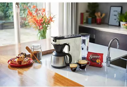 Keuken met een koffiezetapparaat en eten. Een raam op de achtergrond zorgt voor natuurlijk licht.