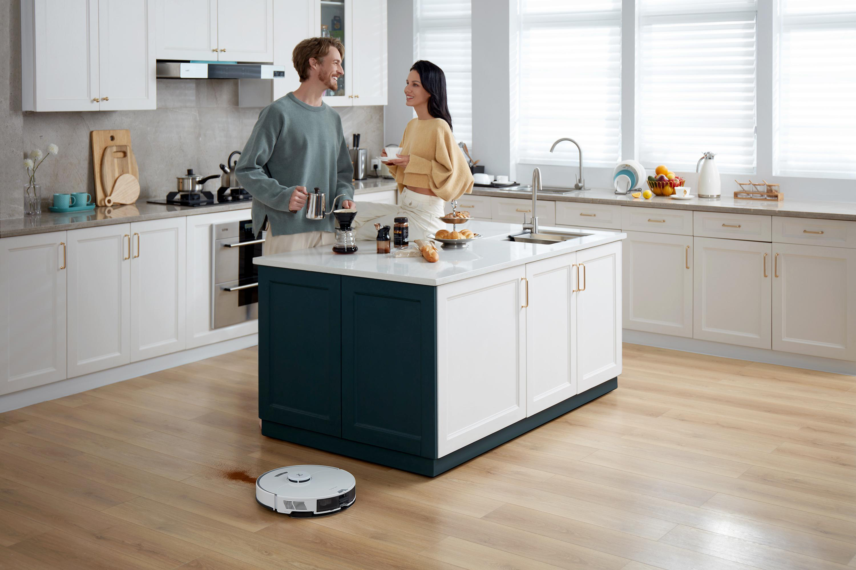 Paar in Küche mit Roboter-Staubsauger auf dem Boden.