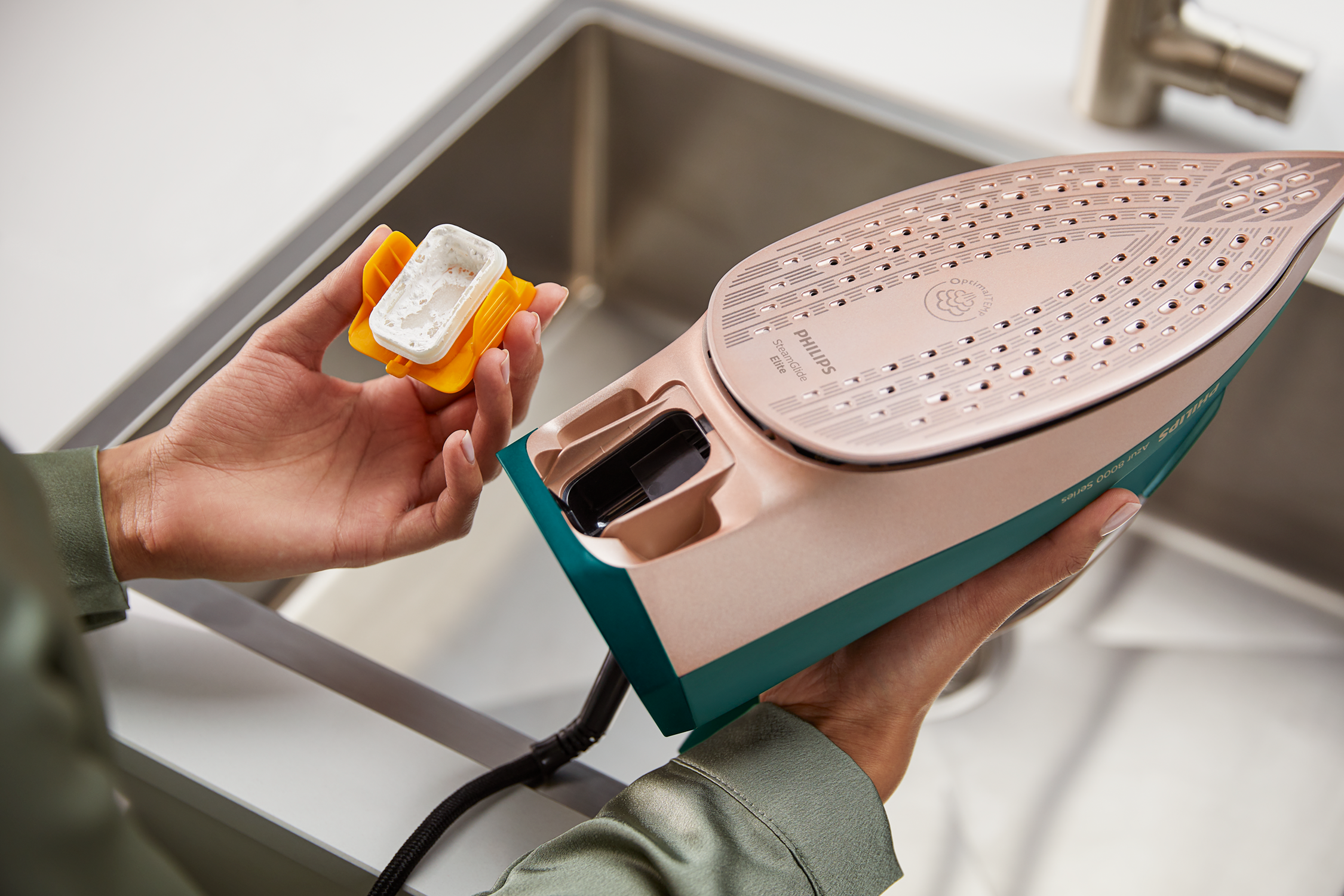 A person's hands holding a teal and rose gold iron. The person is adding water.