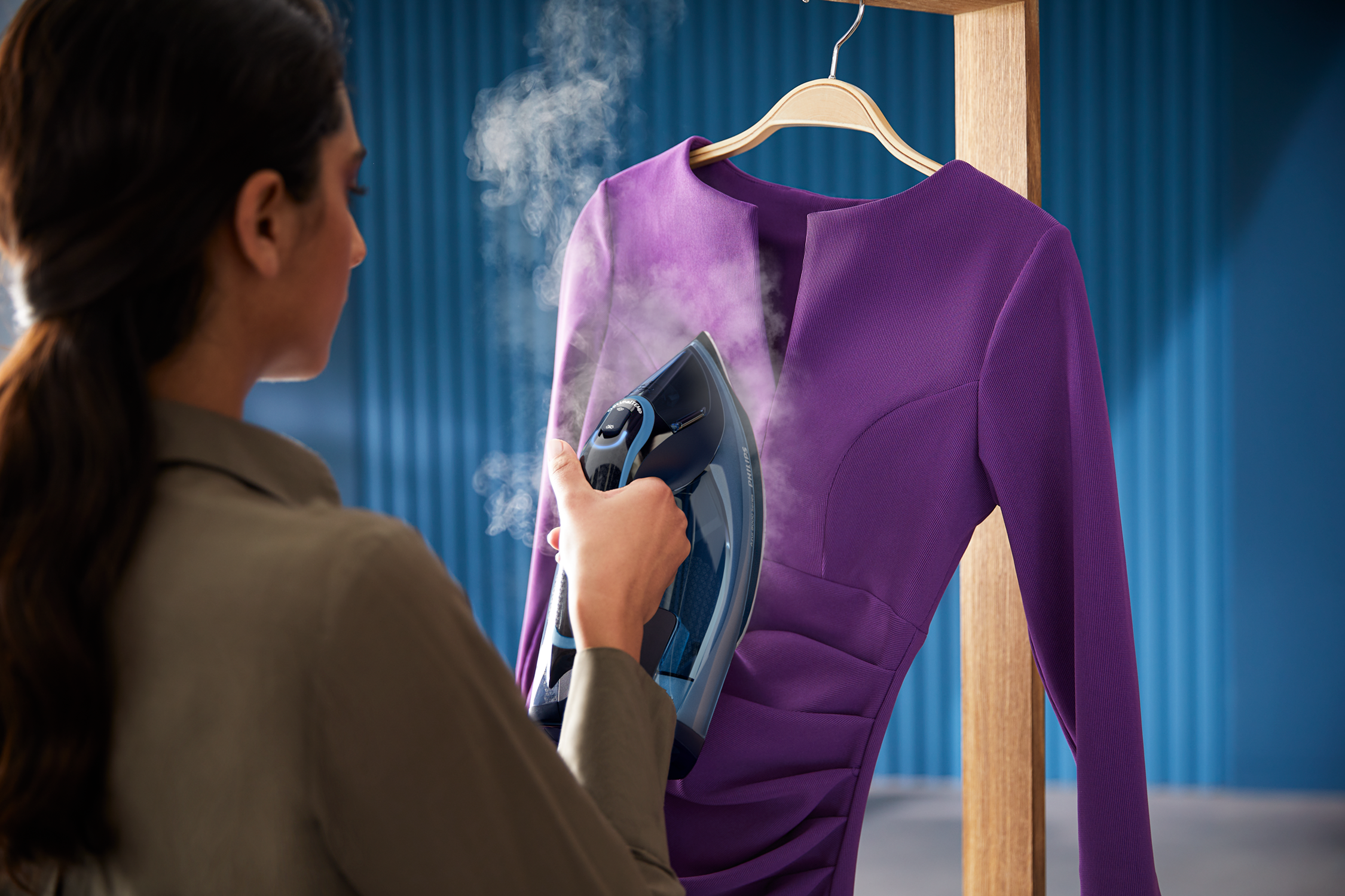 Woman ironing a purple dress on a wooden stand, steam visible, blue background.