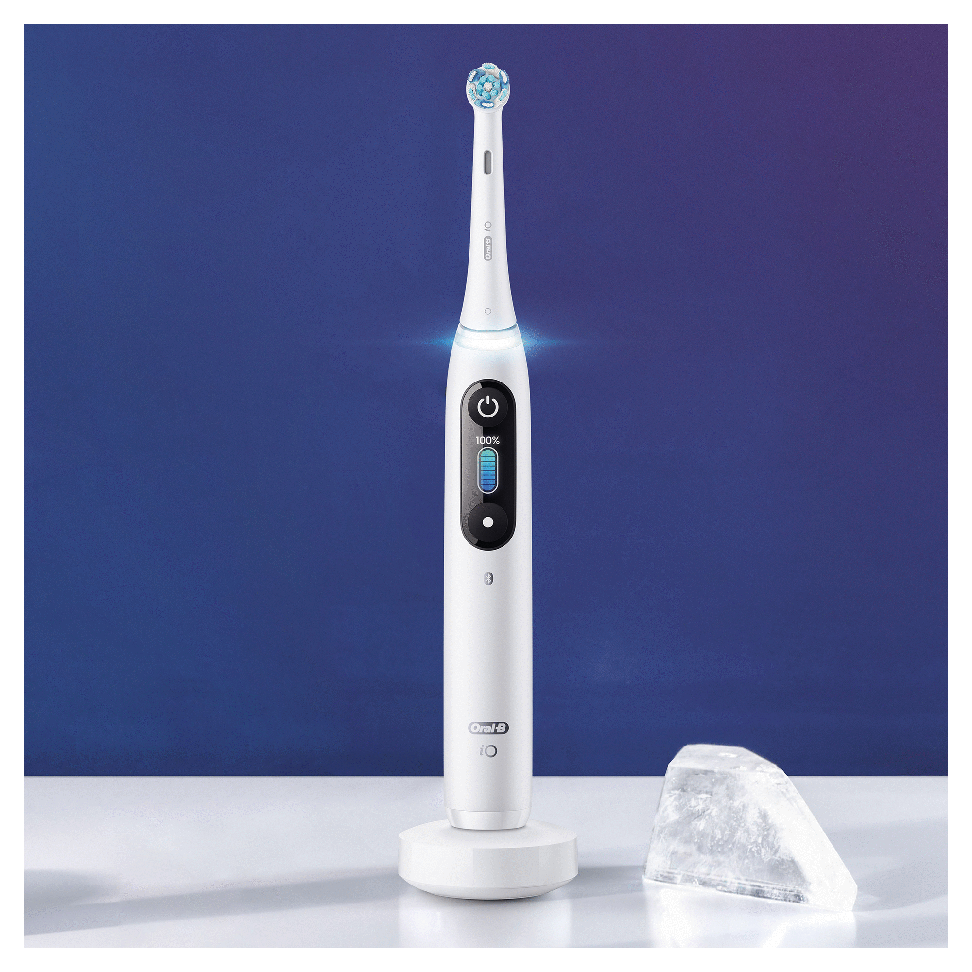 White electric toothbrush on a stand. Shows battery level. Ice cube next to it. Blue background.