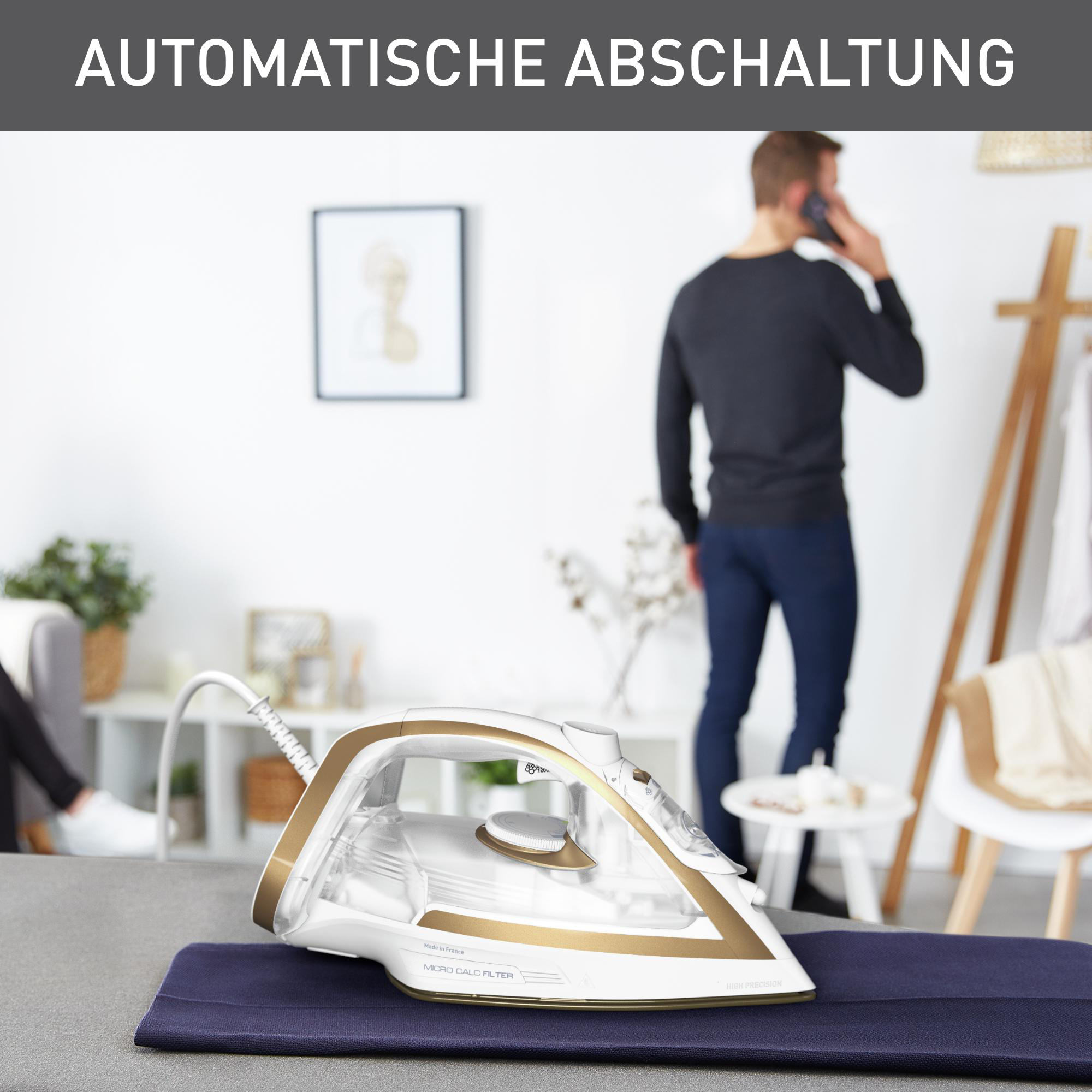 Ein Bügeleisen auf einem Brett mit einer Person am Telefon im Hintergrund.