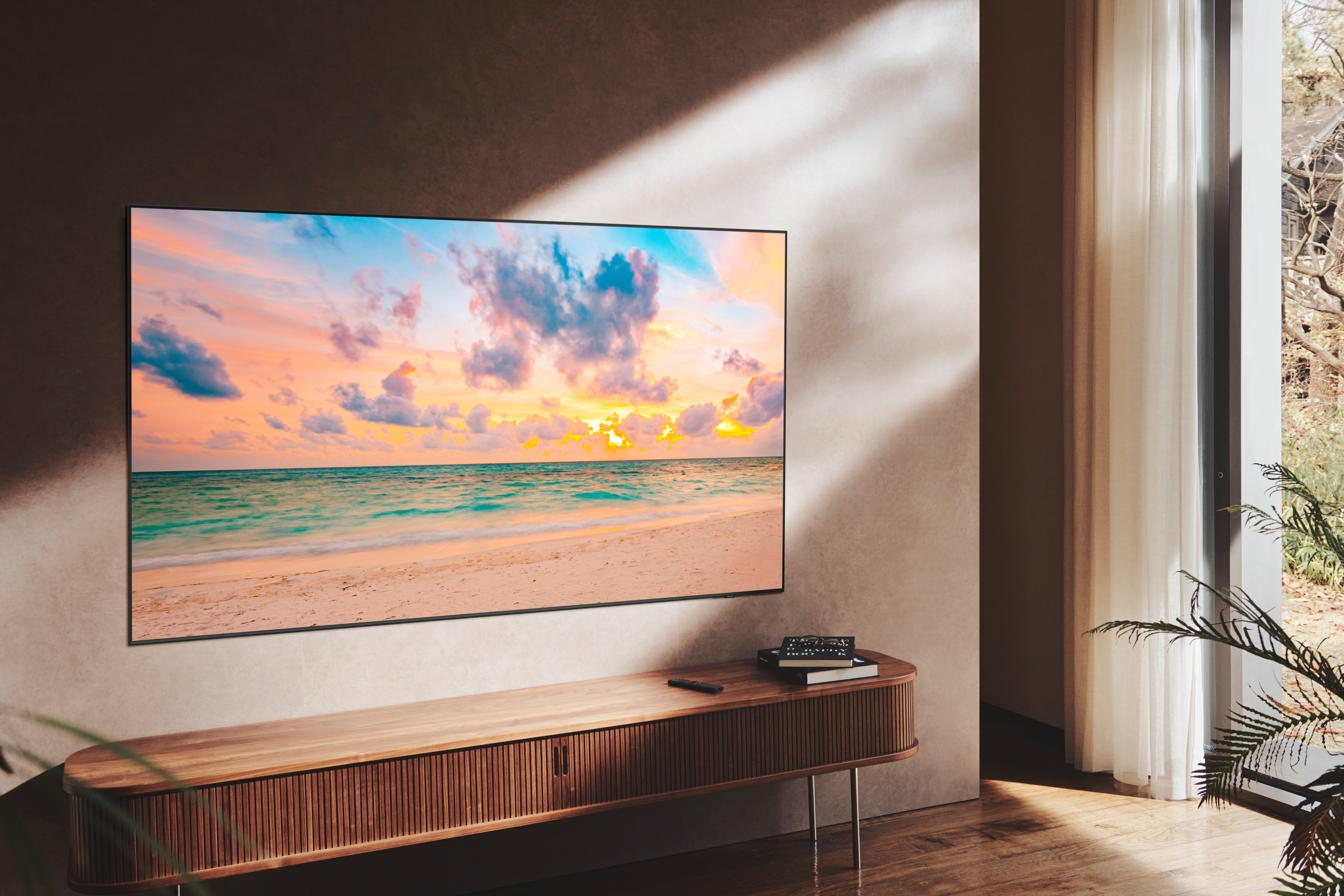 TV mostrando escena de playa, sobre consola de madera, contra pared.