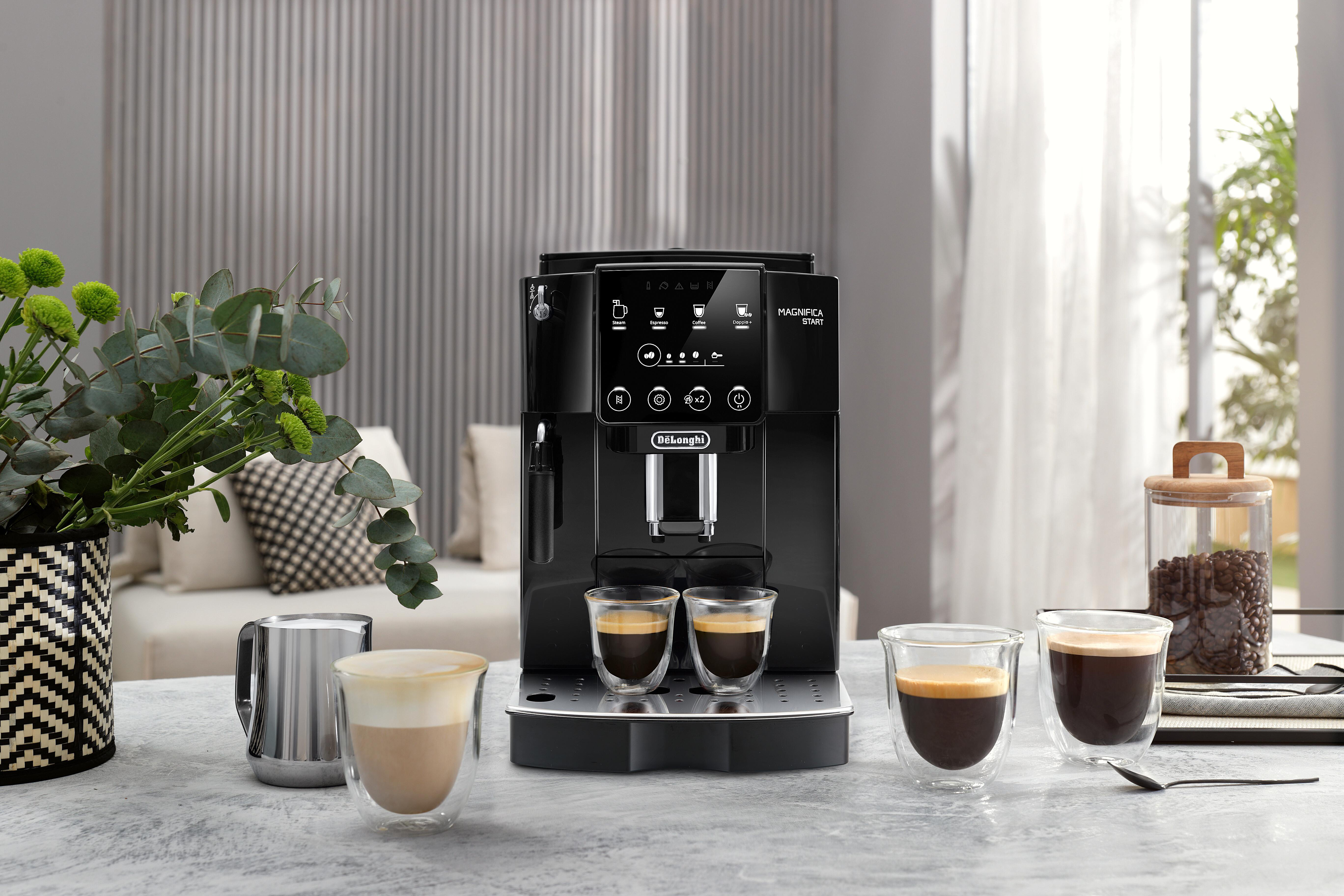 Schwarze Kaffeemaschine auf einem Tisch mit Kaffeetassen und einer Vase mit Pflanzen.