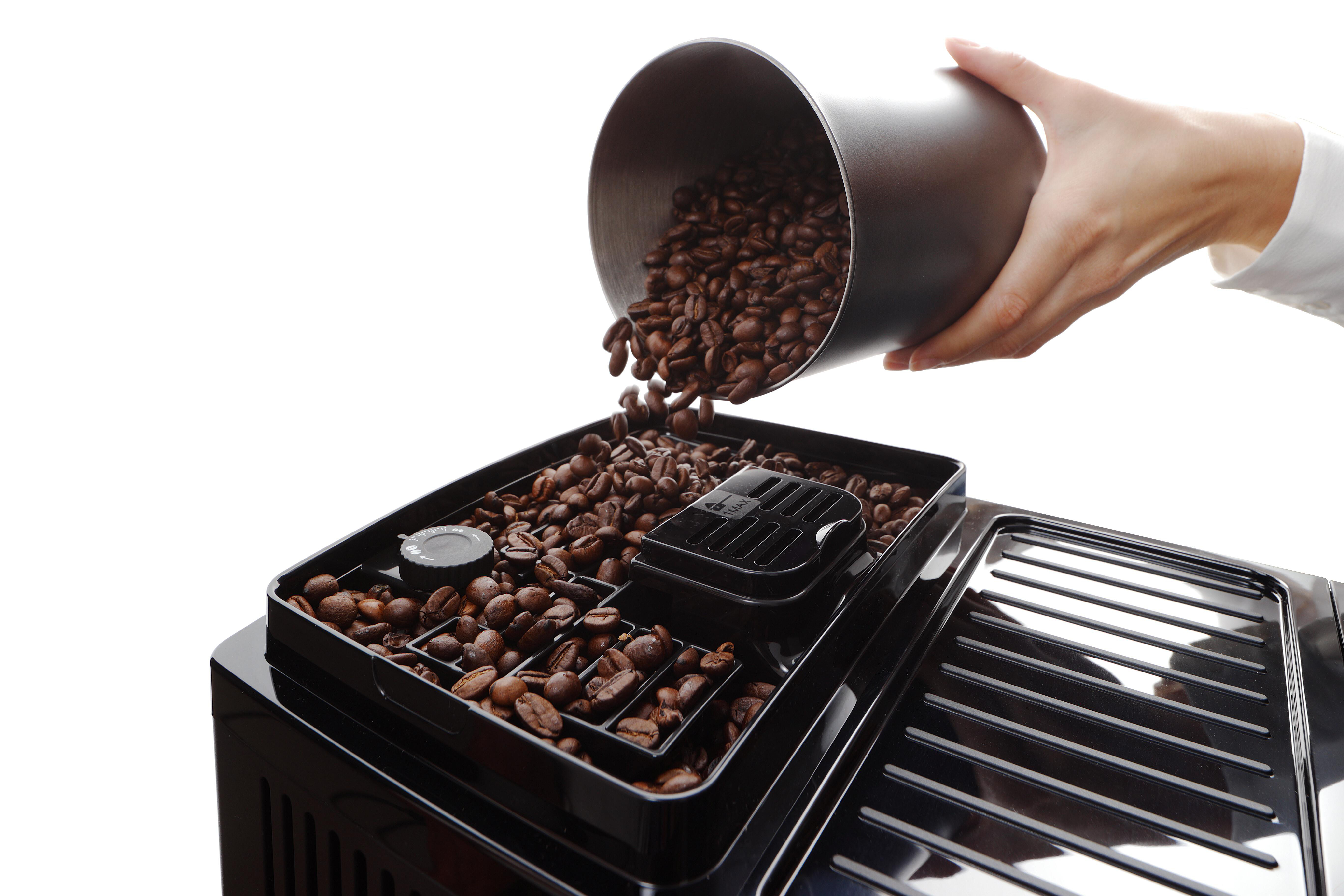 Eine Hand schüttet Kaffeebohnen in eine Kaffeemaschine. Schwarze Maschine, weißer Hintergrund.