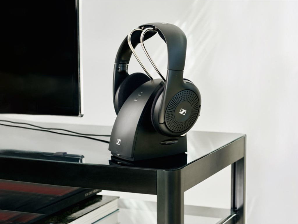 Black headphones on a charging dock on a black surface, with books.