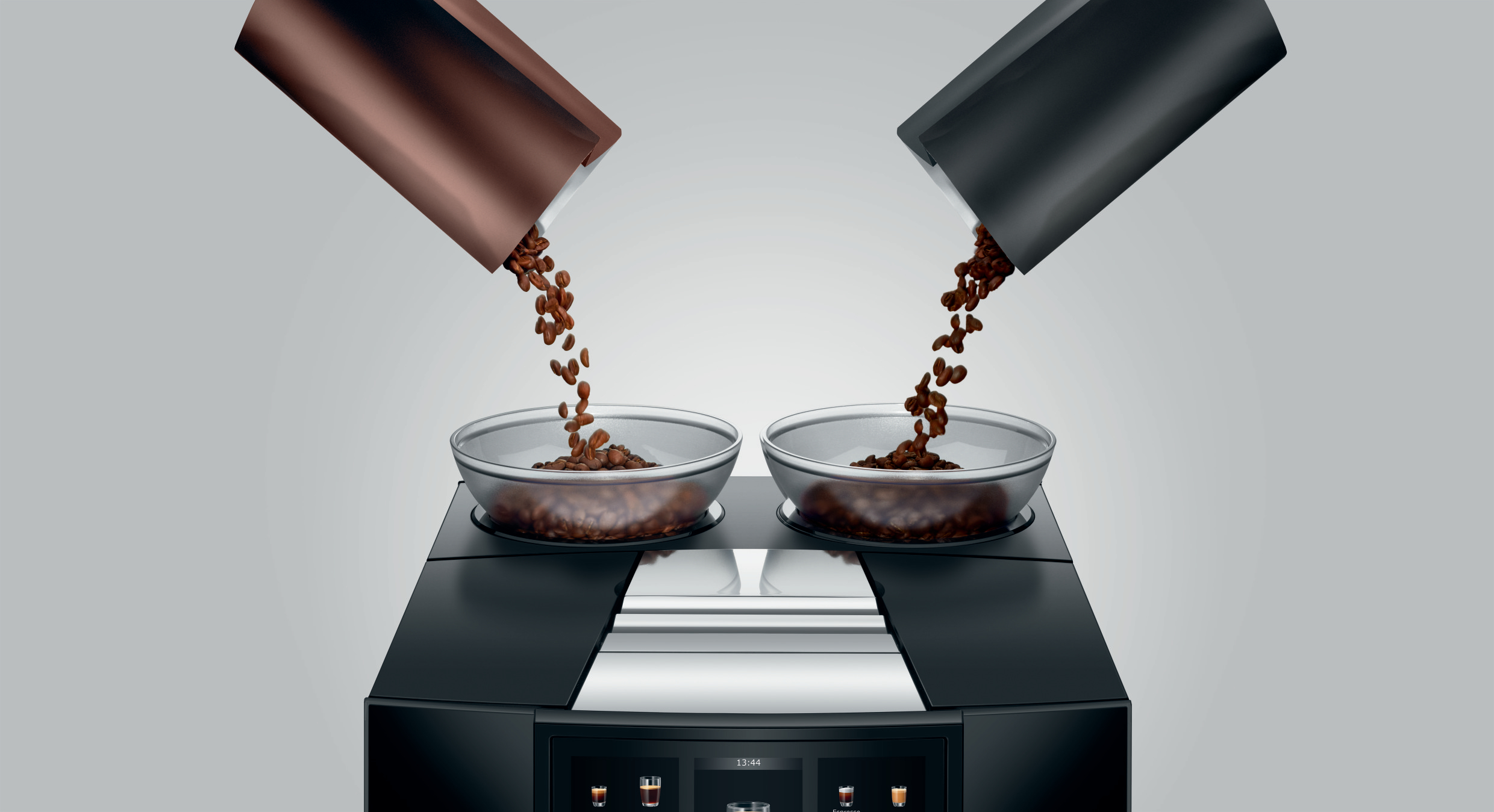 Kaffeebohnen, die aus braunen und schwarzen Behältern in zwei Glasschalen fließen.