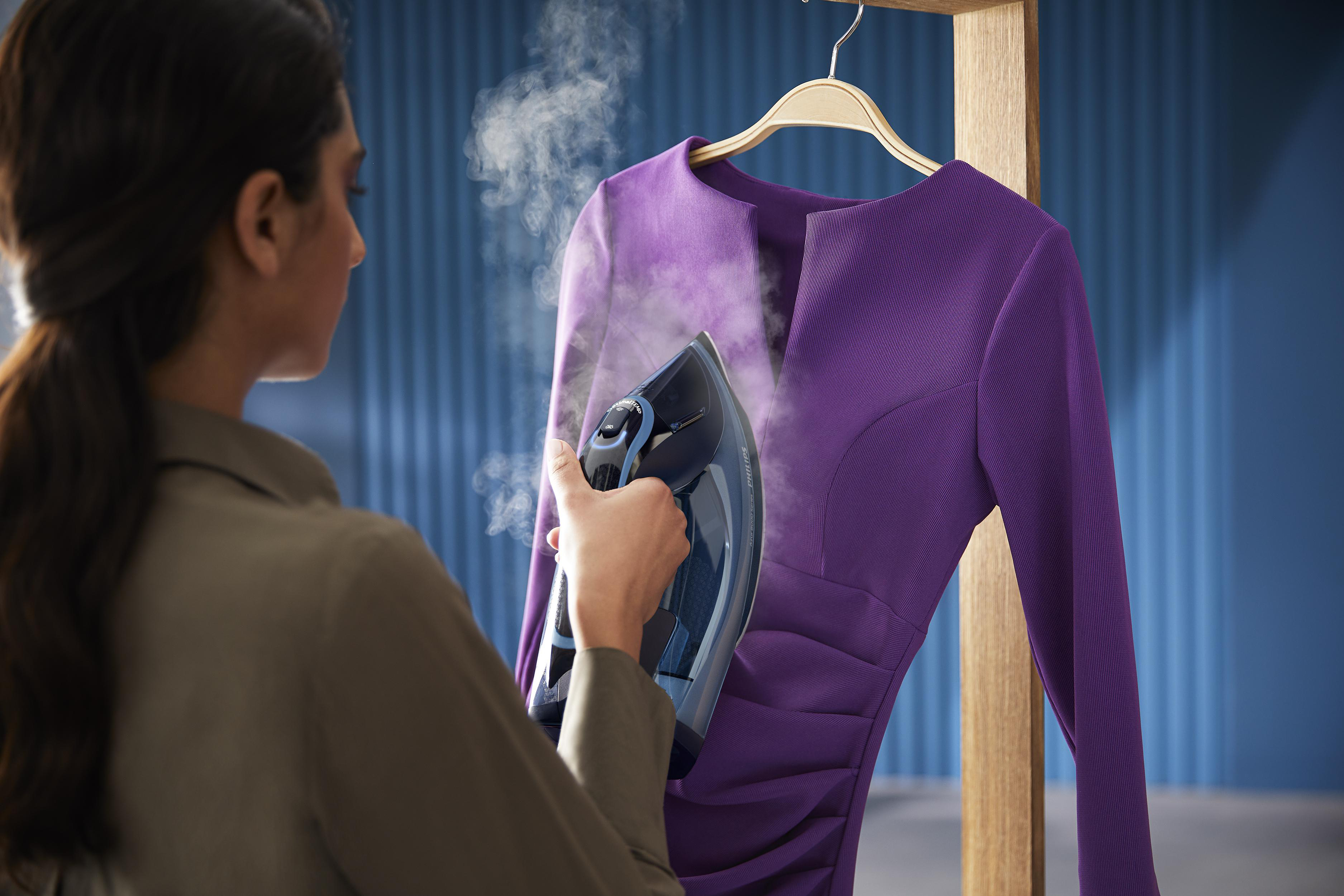 Frau, die ein lila Kleid auf einem Holzbügel mit einem Bügeleisen dampft.