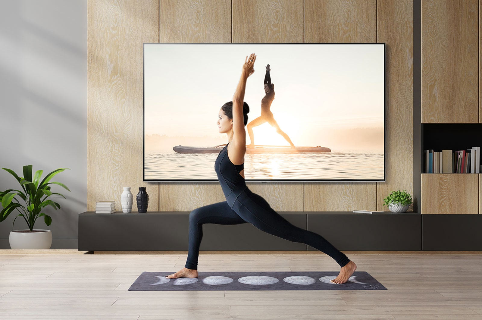Yoga sahnesi gösteren bir TV ekranının önünde yoga pozu yapan bir kadın.