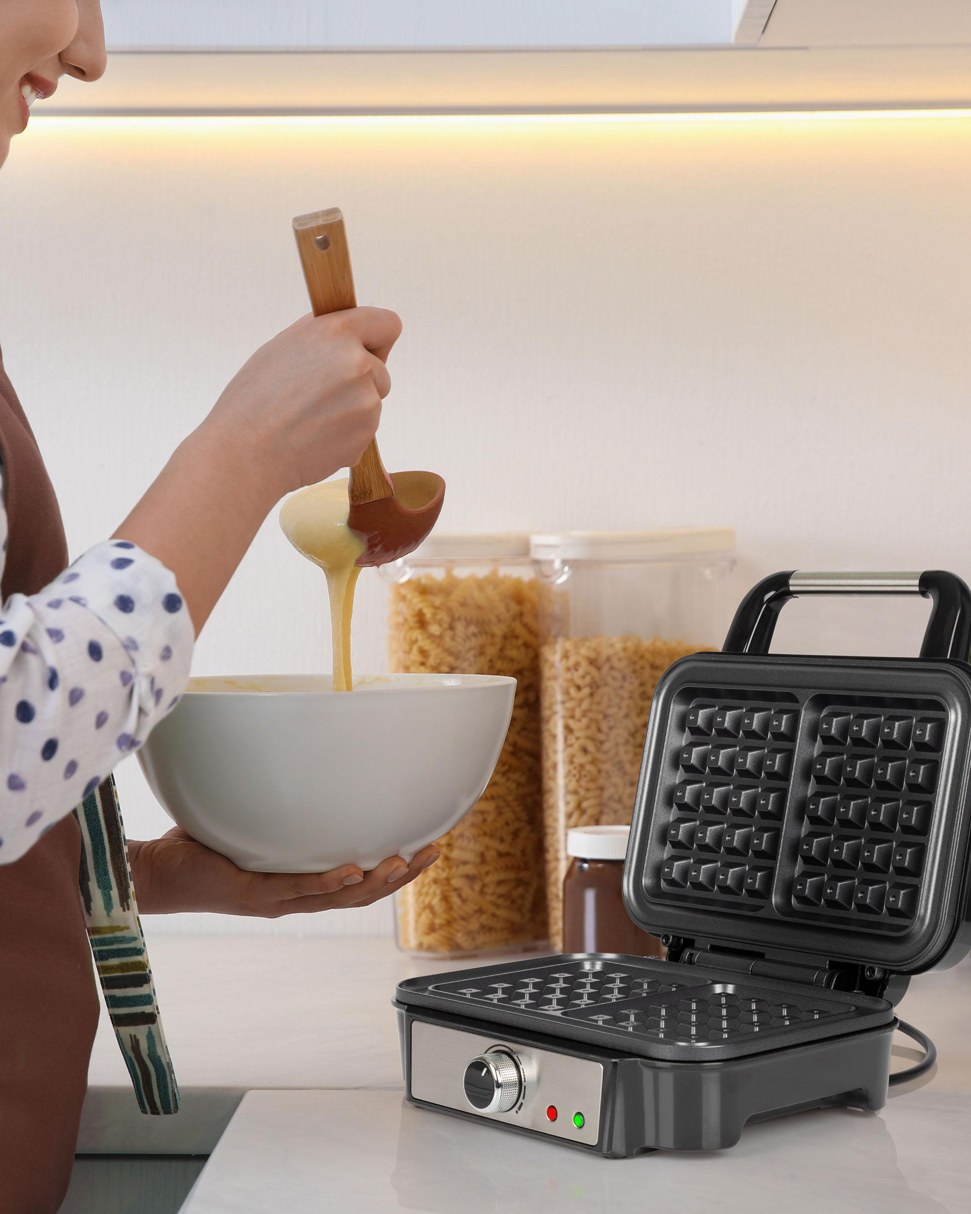 Eine Frau gießt Teig in einen Waffeleisen auf einer Küchentheke.