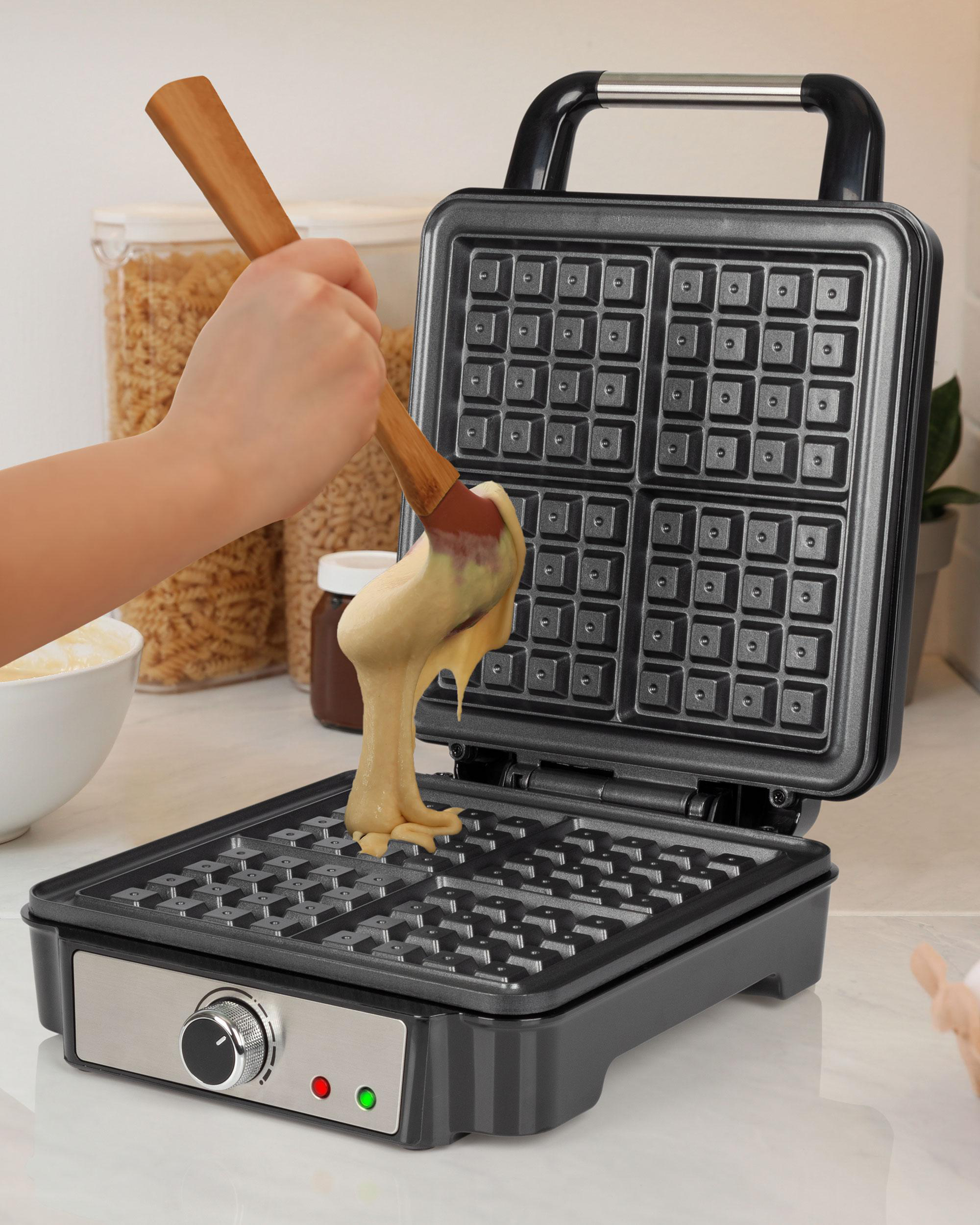 Eine Person gießt Teig mit einem Holzlöffel in ein Waffeleisen. Das Eisen ist offen.