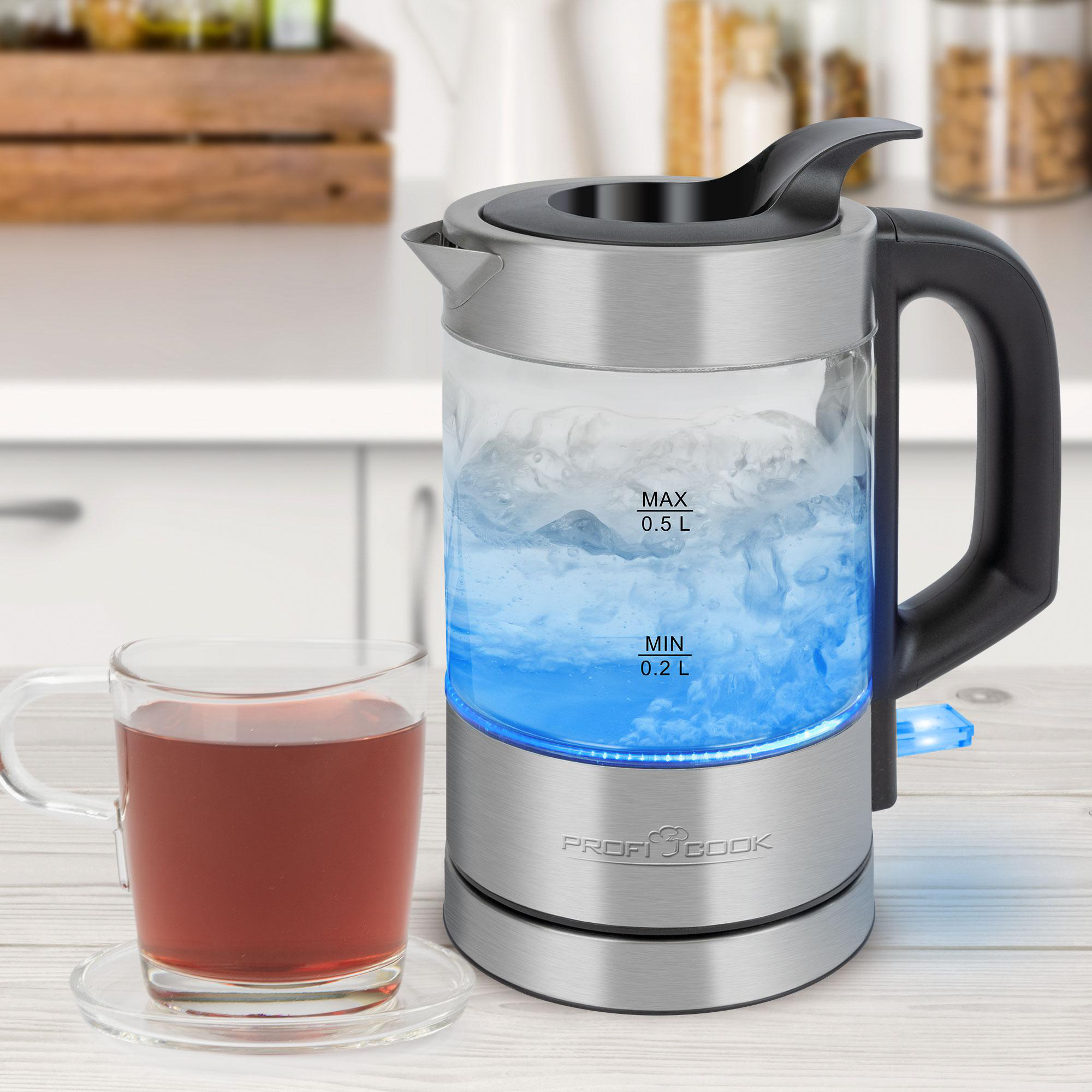Ein elektrischer Glaskessel mit kochendem Wasser, eine Tasse Tee und eine Holzoberfläche.
