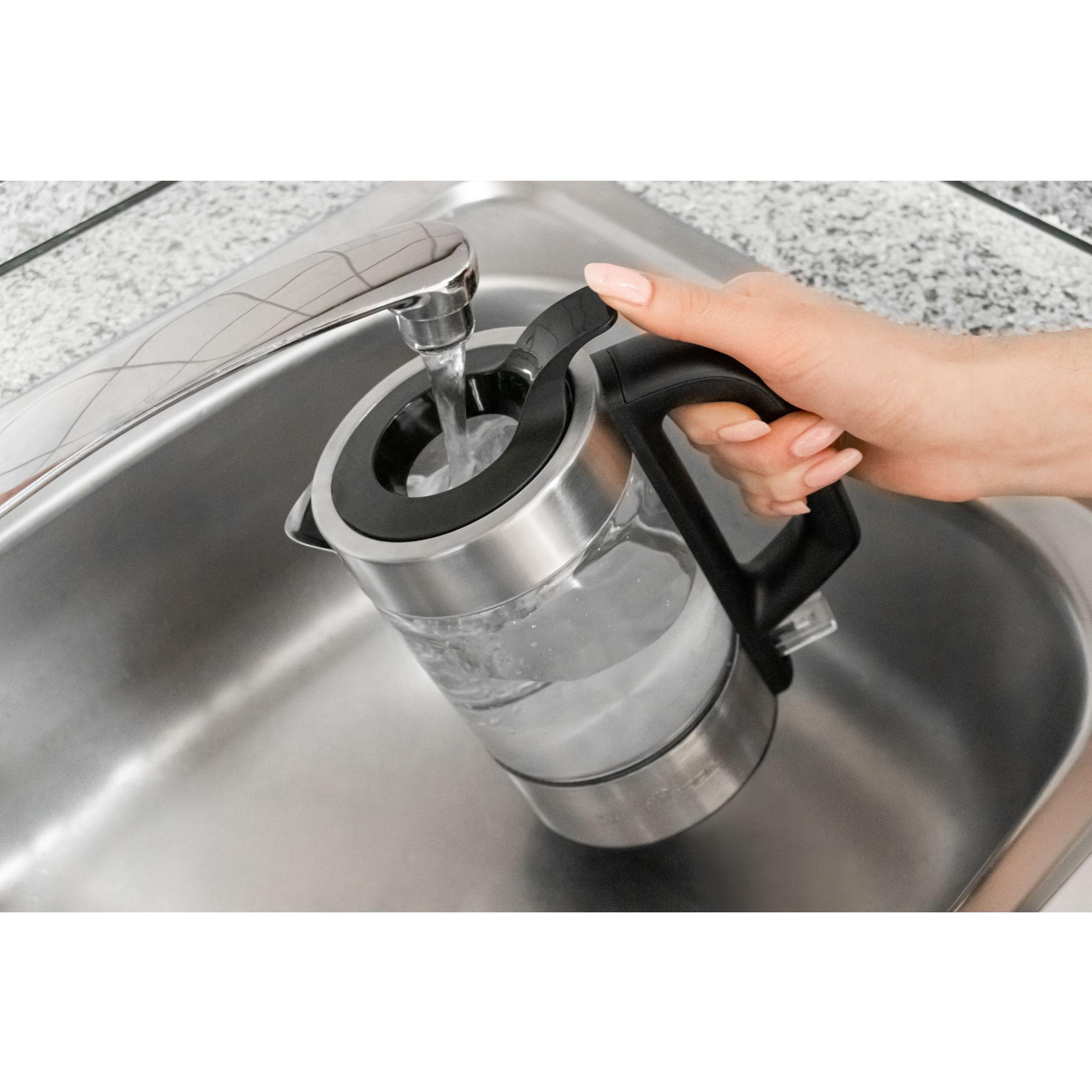 Die Hand einer Person füllt einen elektrischen Glaskessel mit Wasser aus einem Wasserhahn.