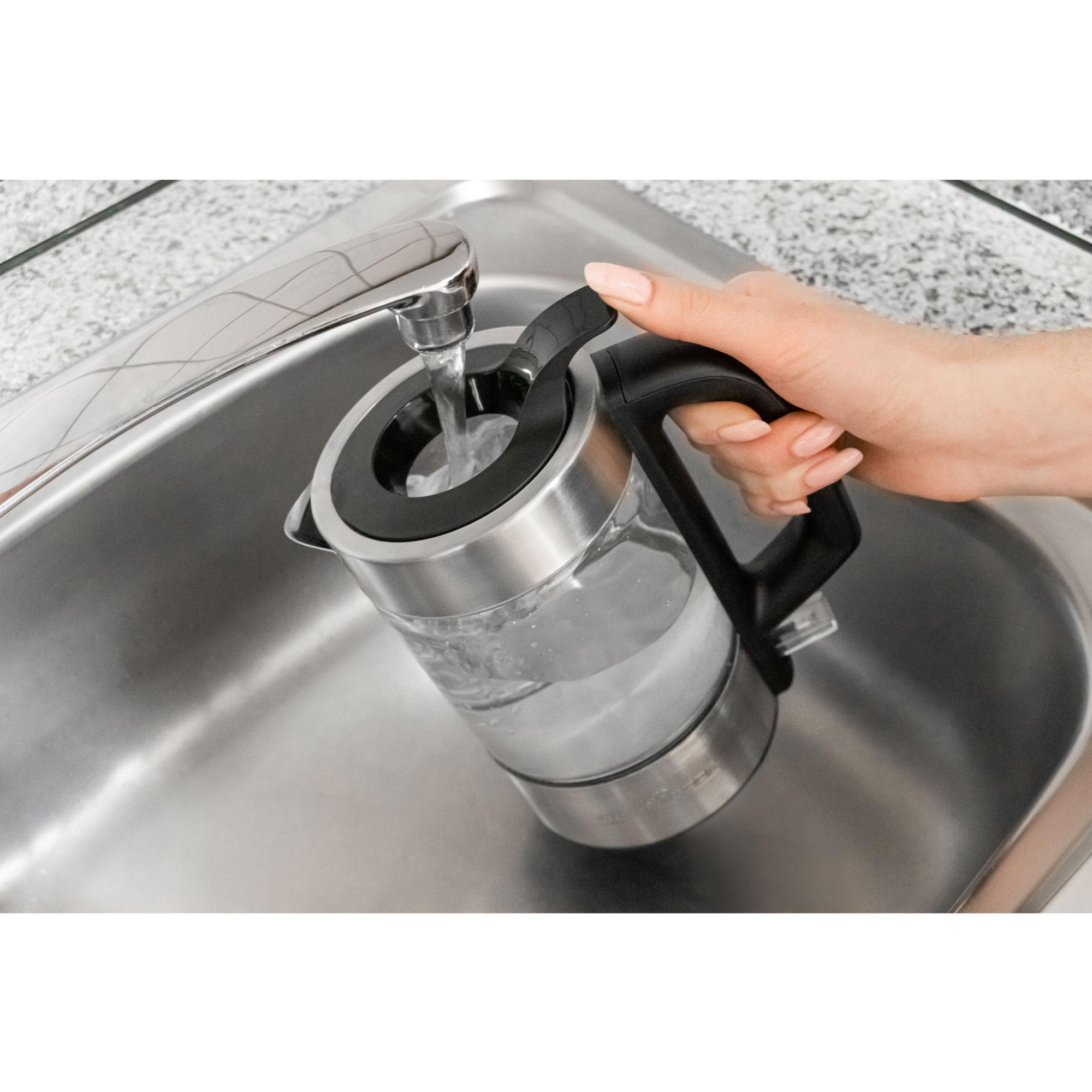 Eine Person füllt einen silbernen Wasserkocher mit Wasser.