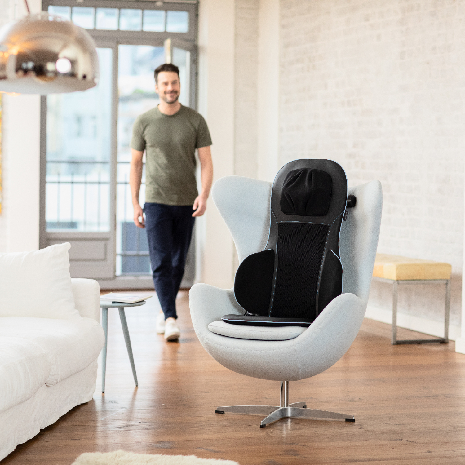 Homme s'approchant d'un fauteuil œuf avec une chaise de massage noire.