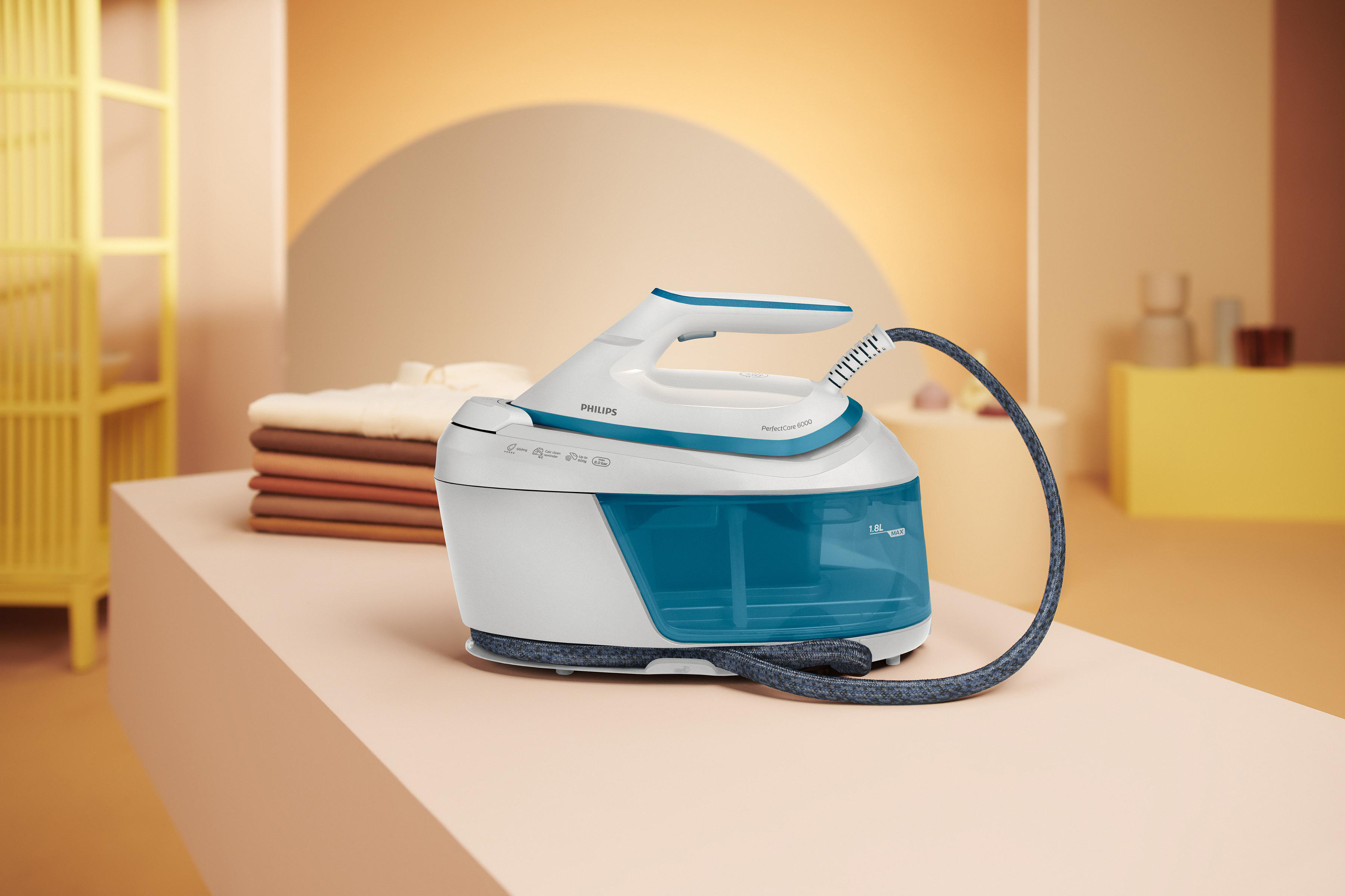 Ein weiß-blaues Philips-Bügeleisen mit Wassertank, Dampfschlauch und einem Stapel gefalteter Kleidung.