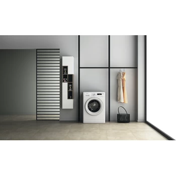 Een wasruimte met een wasmachine. Jurken hangen aan de rechterkant.