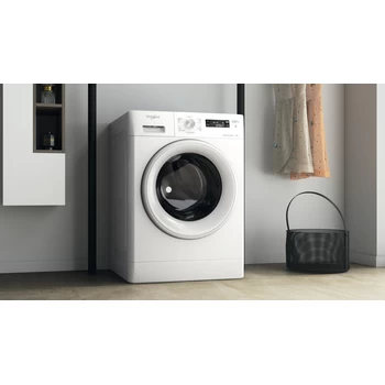 Een witte wasmachine in een kamer, met een zwarte wasmand en hangende jurken.