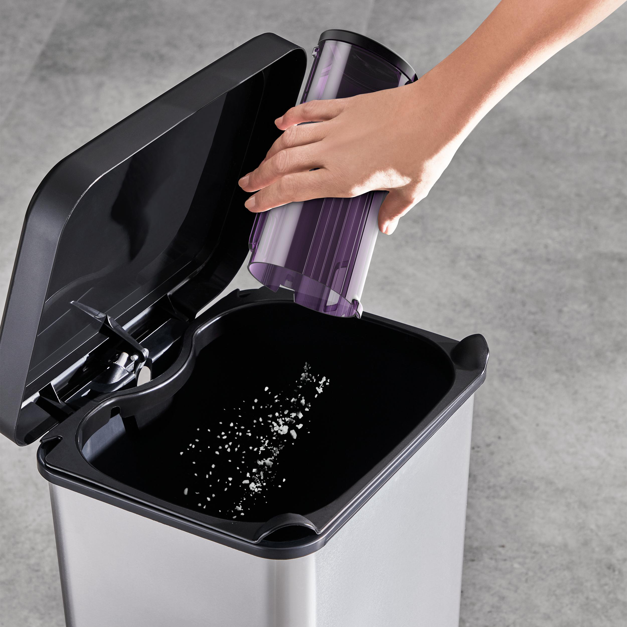 Eine Hand, die den Inhalt des Staubsaugers in einen Abfalleimer aus Edelstahl leert.