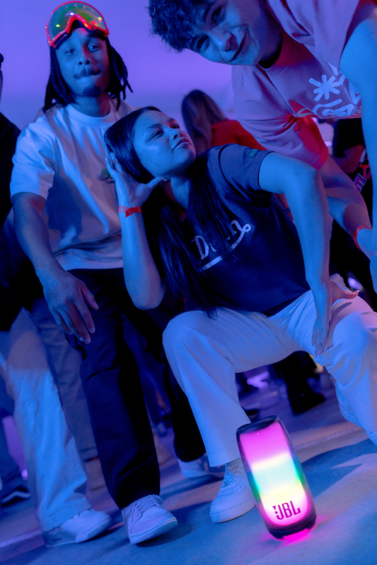 Tanzende Gruppe von Personen in der Nähe eines JBL-Lautsprechers mit Farbwechsel.