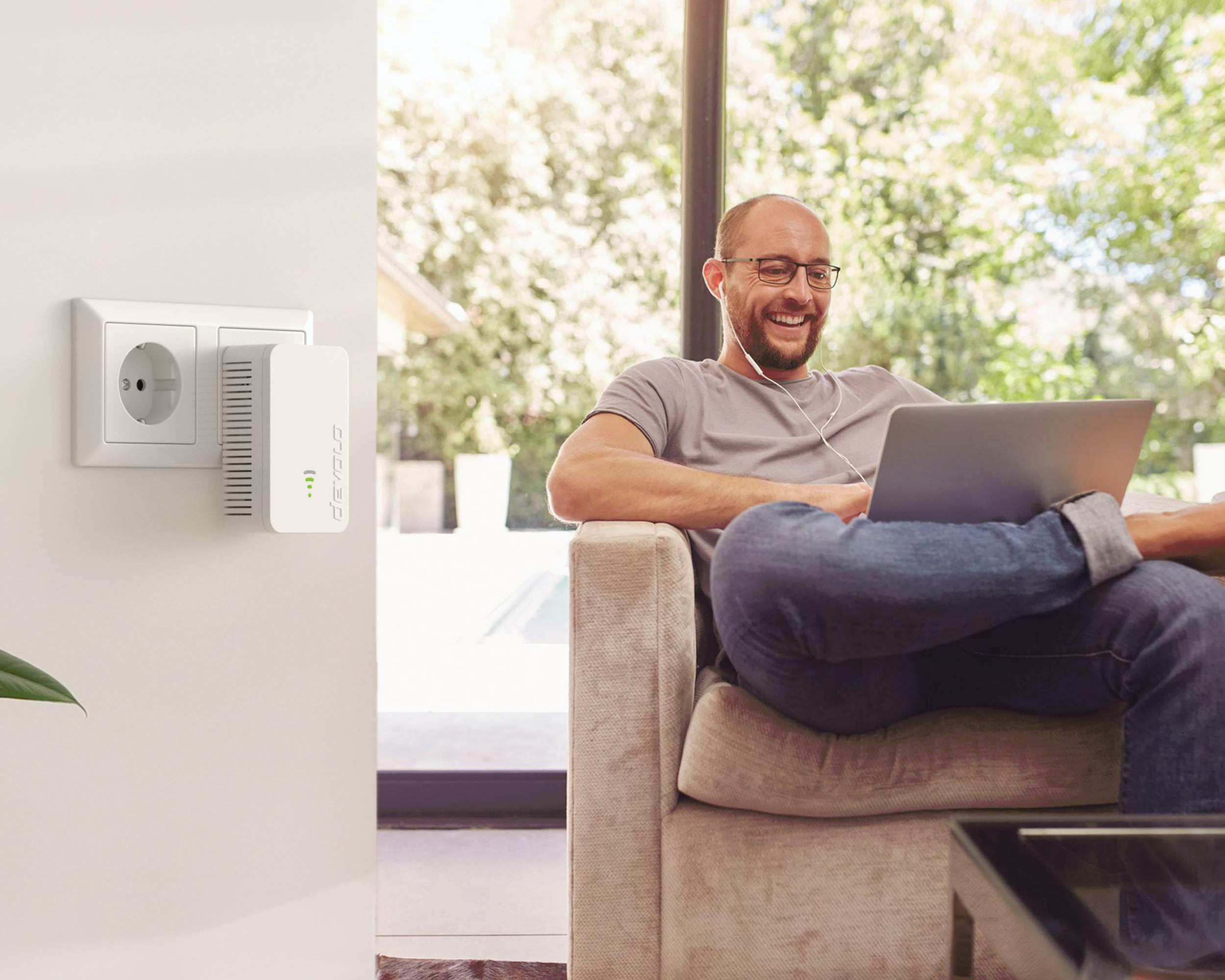 Mann mit Laptop, angesteckter WLAN-Extender an der Wand, heller Hintergrund.