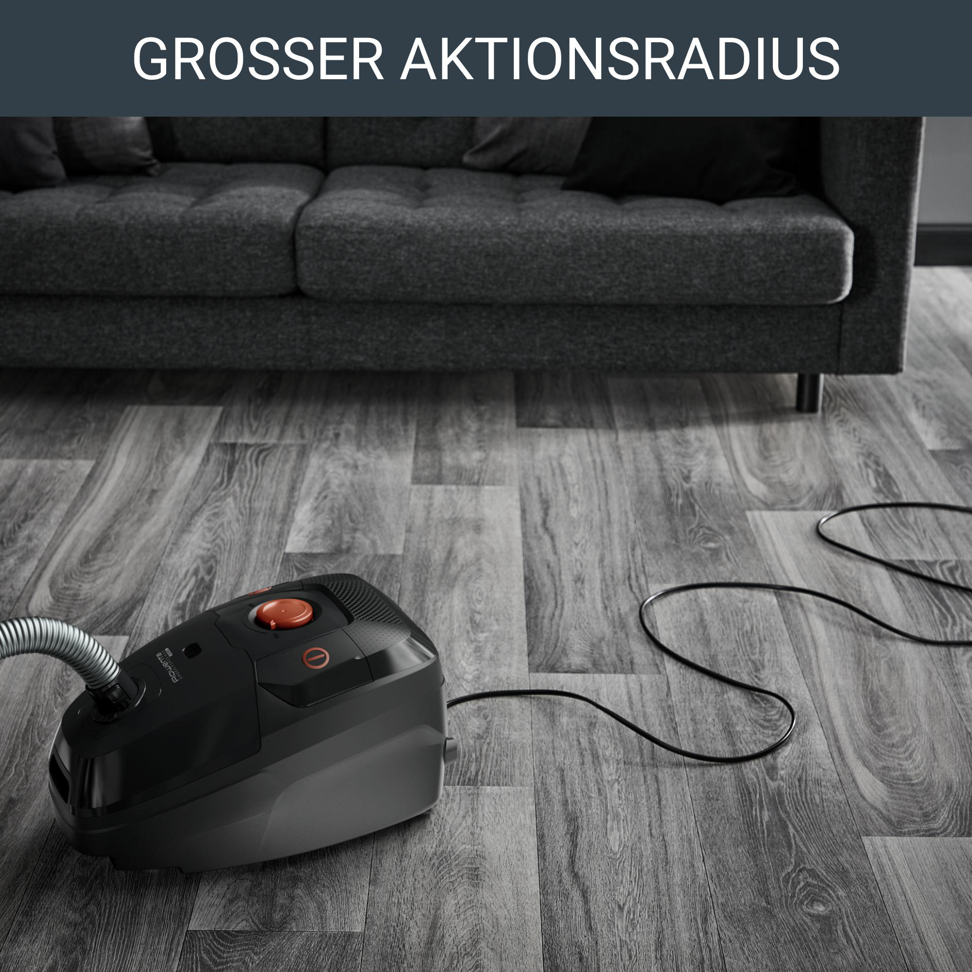 Schwarzer Staubsauger auf grauem Holzboden, in der Nähe eines grauen Sofas.