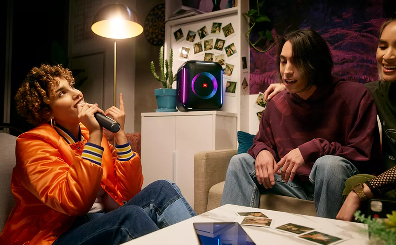 Három ember egy szobában, hangszóróval, karaoke berendezéssel és képekkel a falon.