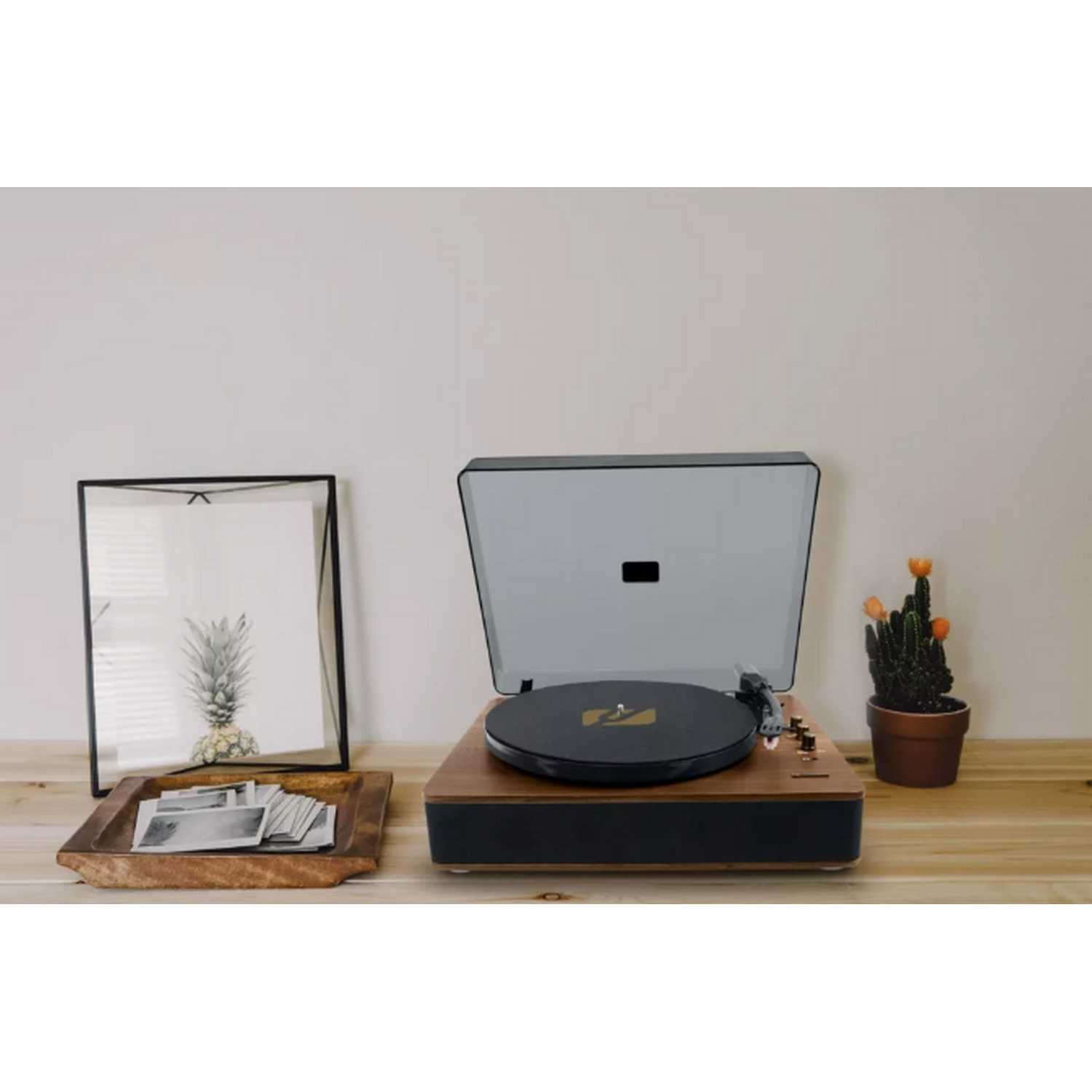 Tocadiscos y arte enmarcado sobre mesa de madera, cactus y decoración.