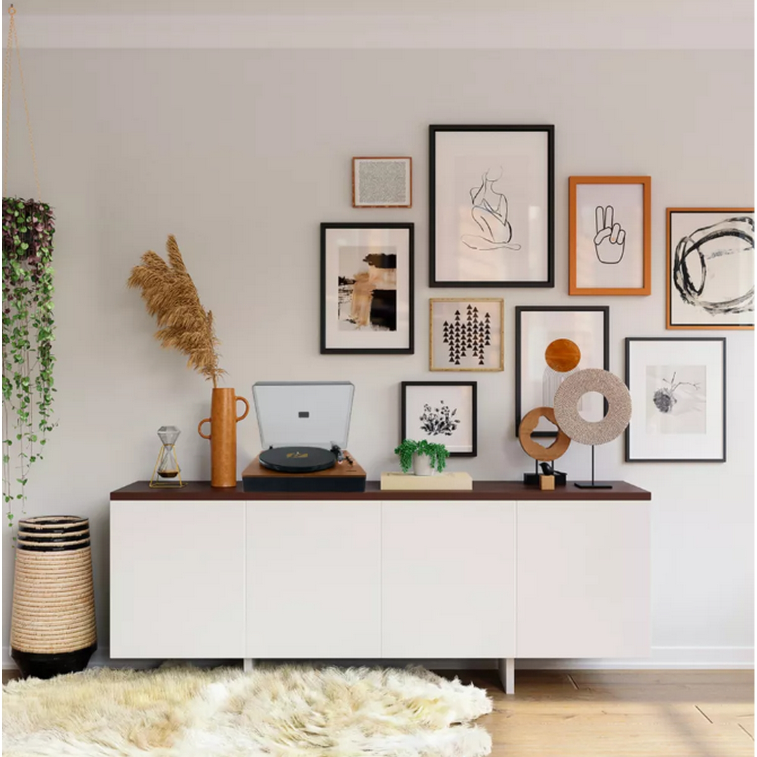 Una exhibición de pared con arte enmarcado, un tocadiscos y objetos decorativos en un gabinete blanco y marrón.