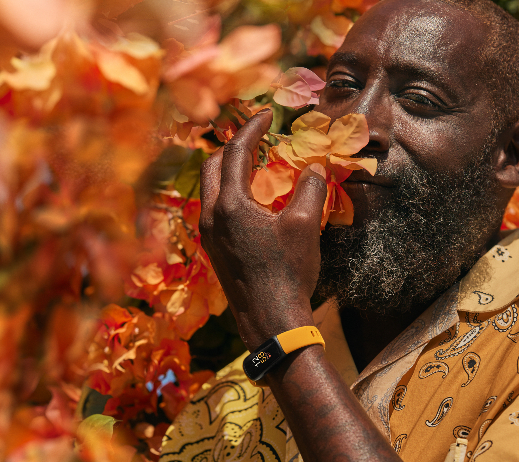 Homme sentant des fleurs, portant une chemise jaune et un tracker de fitness jaune et noir.