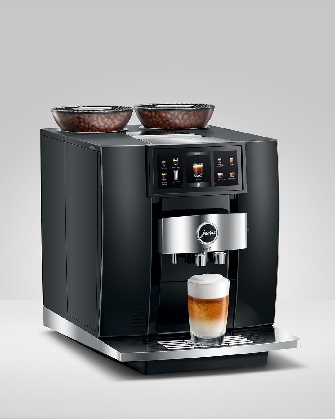Eine schwarze und silberne Jura Kaffeemaschine. Ein Glas Latte davor. Zwei Kaffeebohnenschalen oben.