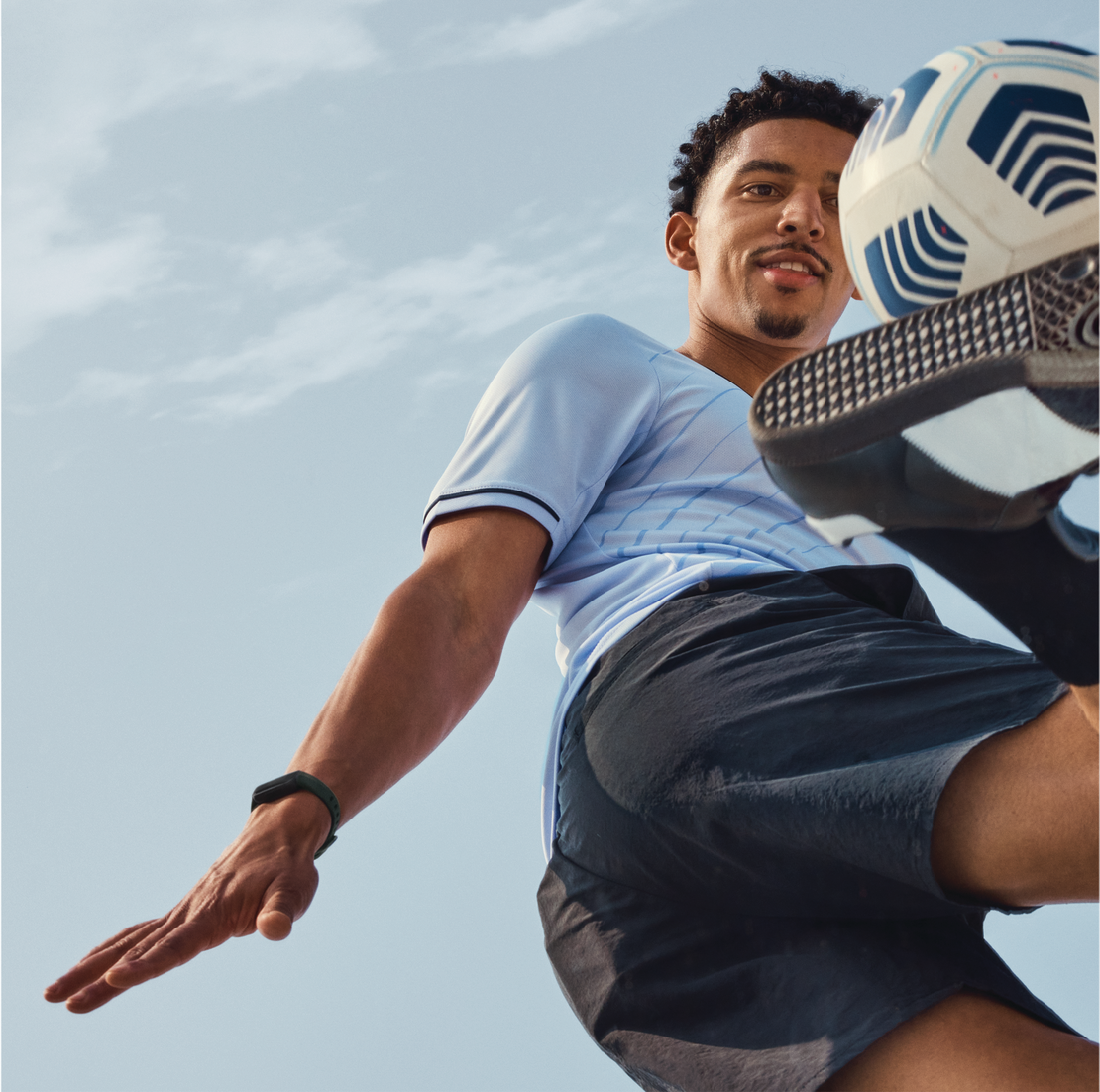 Joueur de foot frappant un ballon en l'air. Ciel en arrière-plan. Vue d'en bas, action et mouvement.