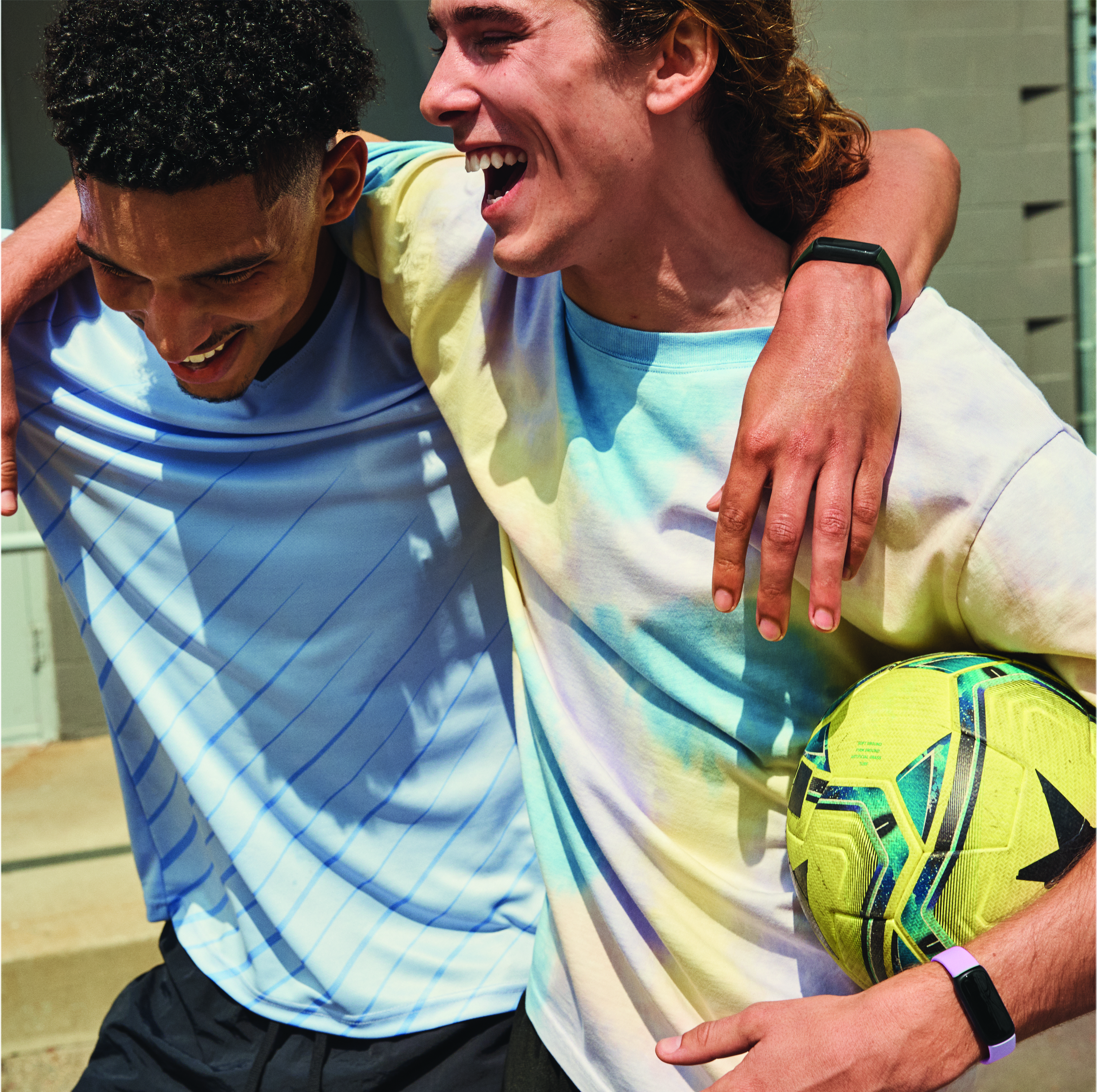 Deux jeunes hommes avec des trackers de fitness au poignet, souriant, tenant un ballon de football.