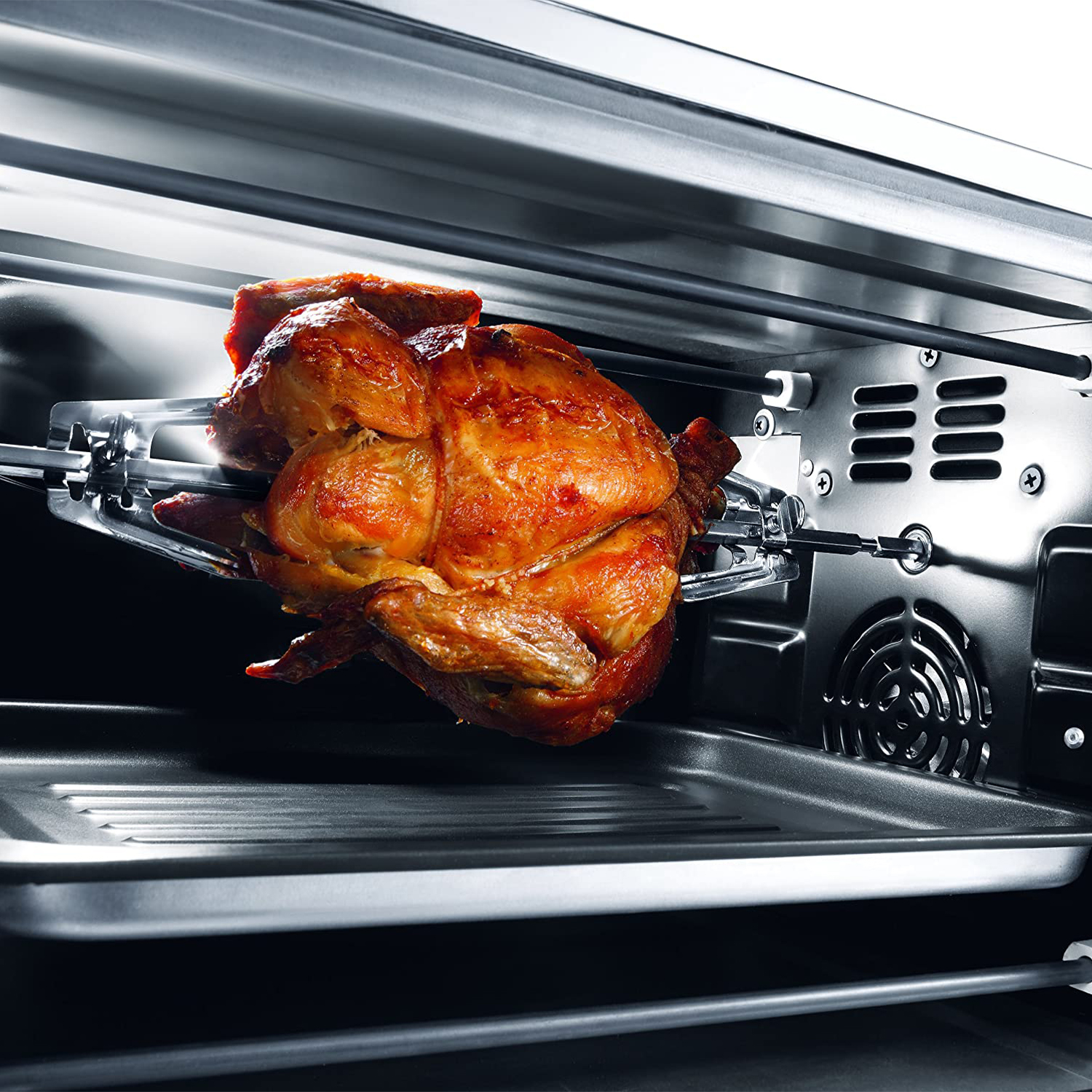 Un pollo arrosto su uno spiedo rotante all'interno di un forno. Il forno è in metallo.