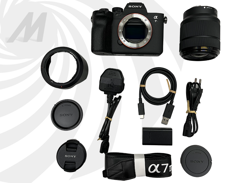 Diverse parti di fotocamera su sfondo bianco: fotocamera, obiettivo, caricabatterie e cavi.