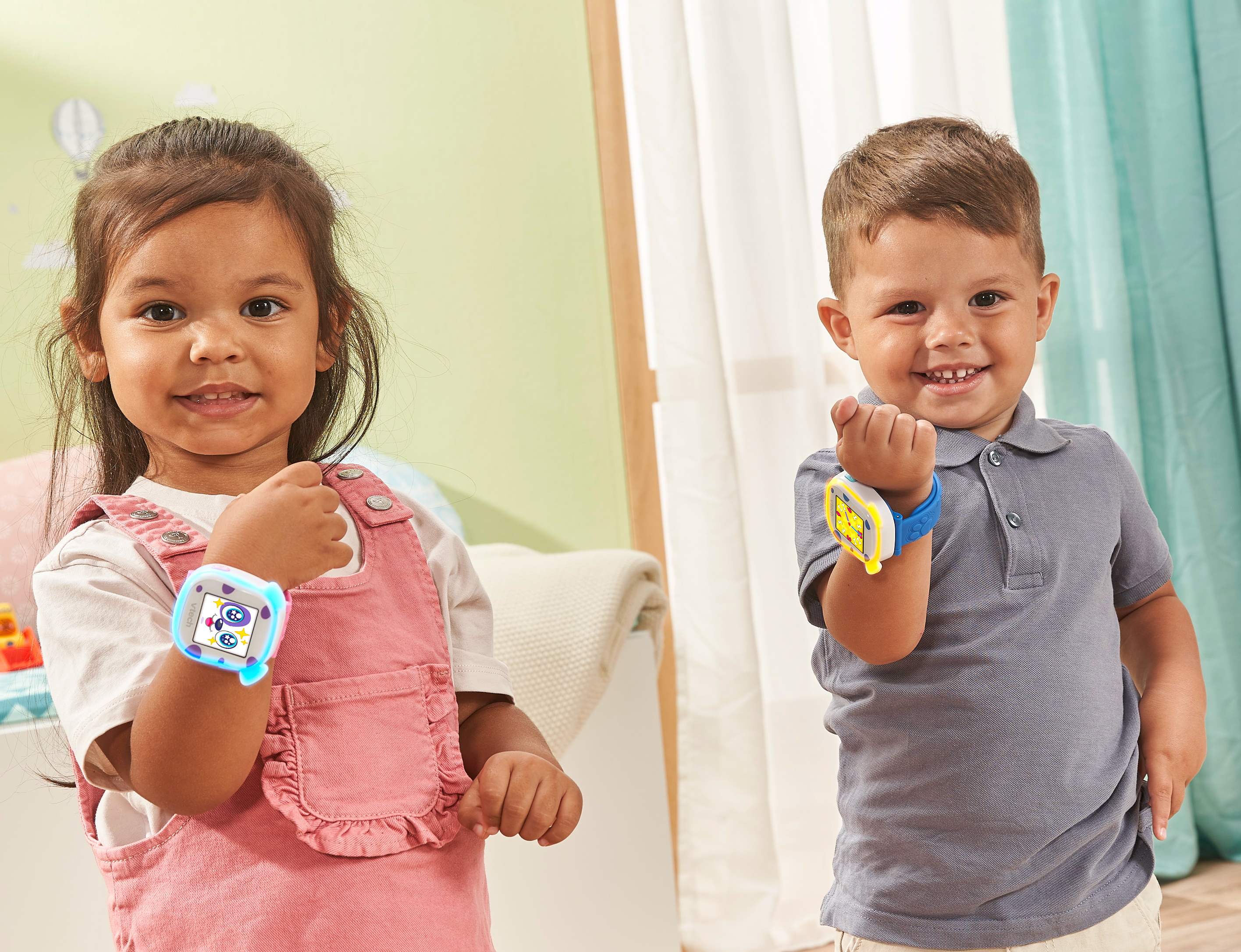 Zwei lächelnde Kinder, die jeweils eine blaue Smartwatch tragen. Text: Vtech.