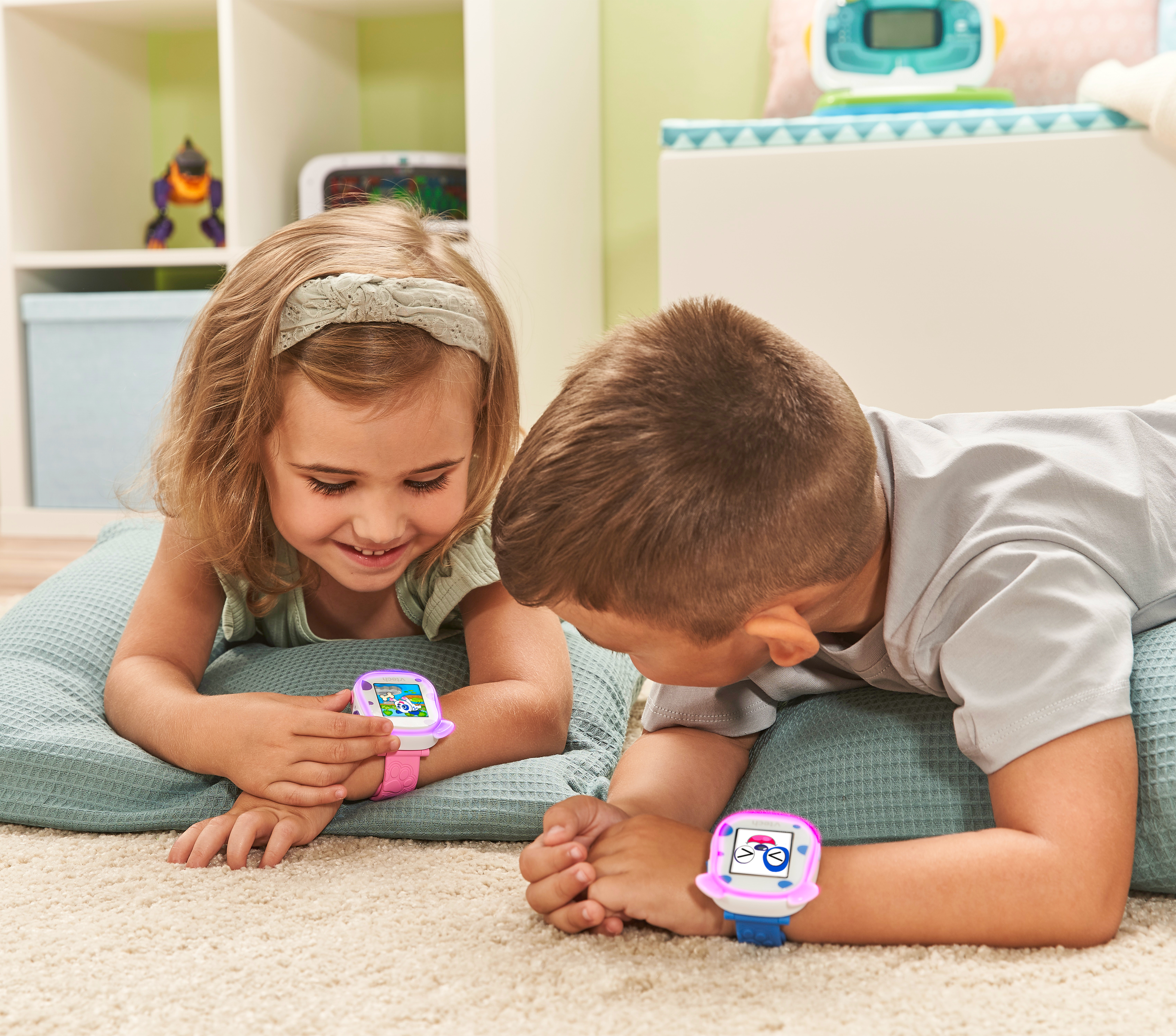 Zwei Kinder mit Smartwatches, lächeln, spielen auf dem Boden.